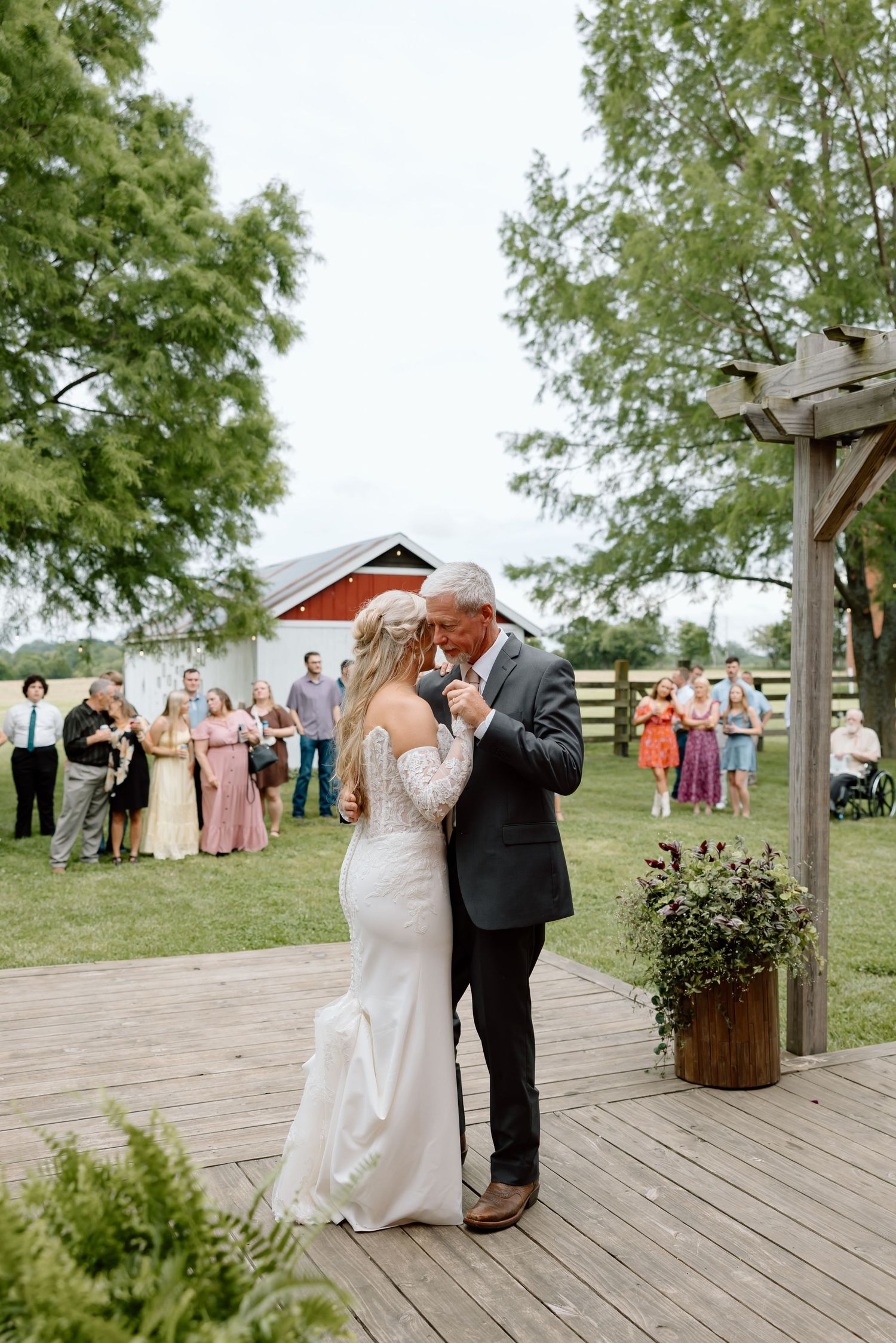 Bride and father share emotional first dance on outdoor wooden deck at rustic barn wedding venue.