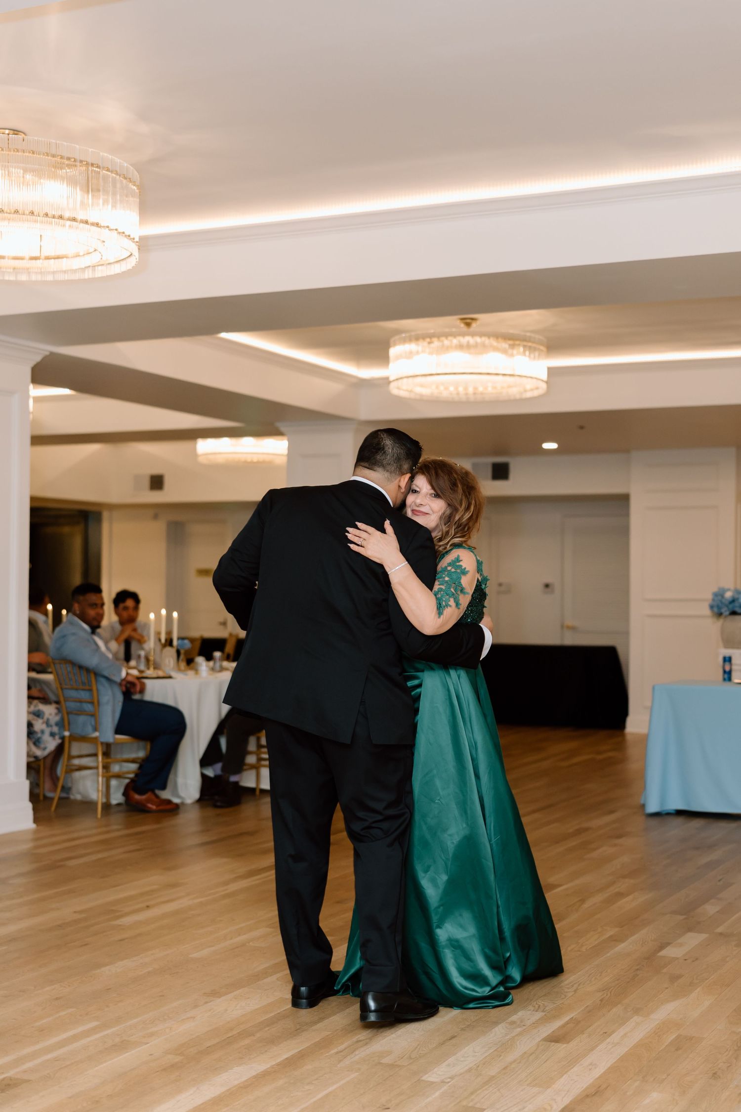 A couple shares an elegant first dance at a wedding reception in a bright ballroom with chandeliers.