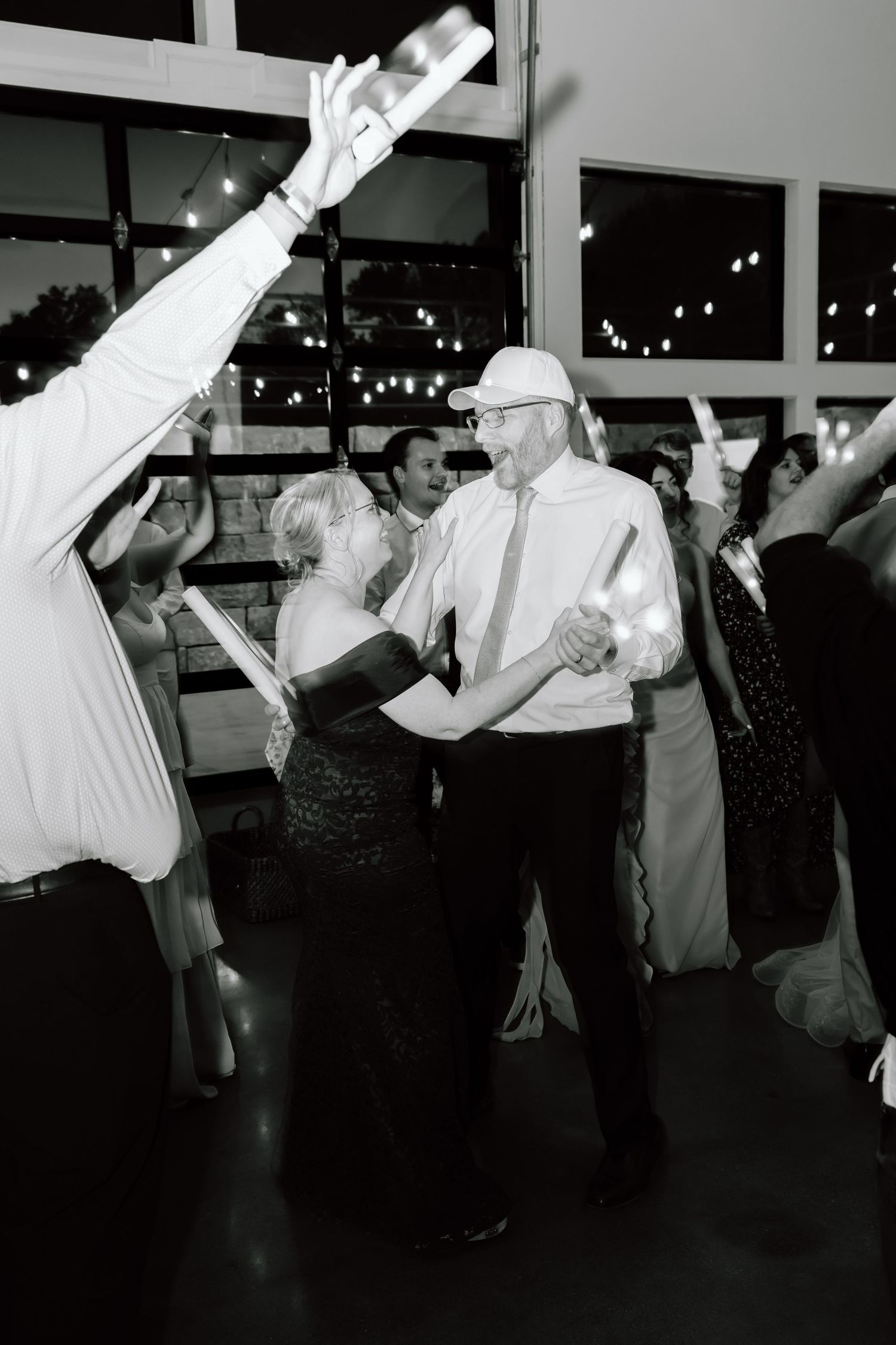 Couple shares a romantic dance surrounded by guests with glow sticks at a lively wedding reception.