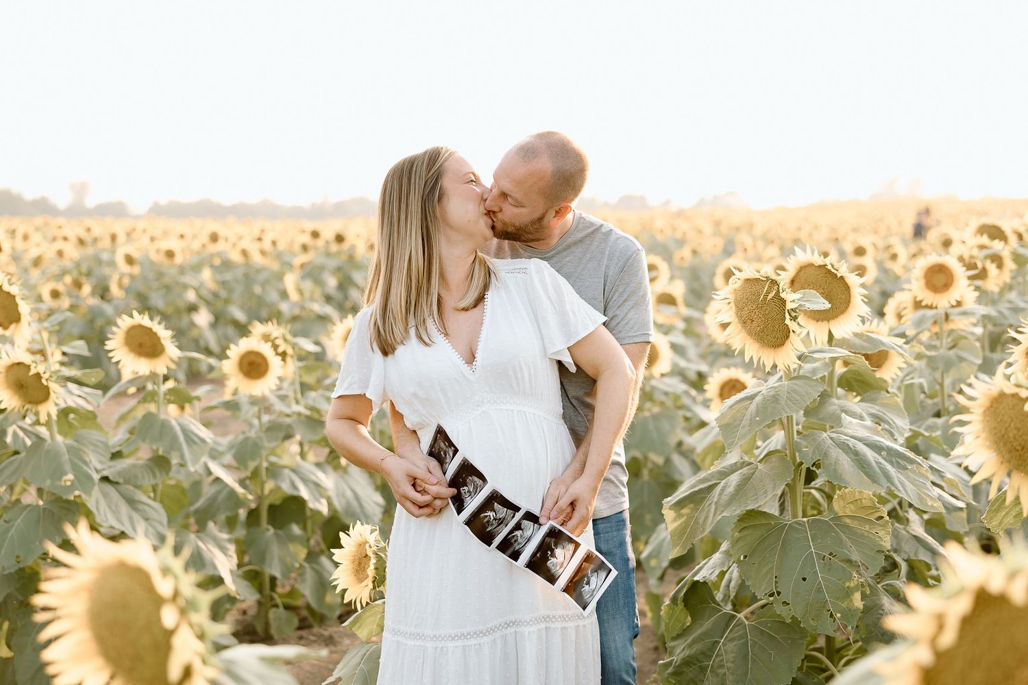 A couple shares an intimate moment in a golden sunflower field during sunset.