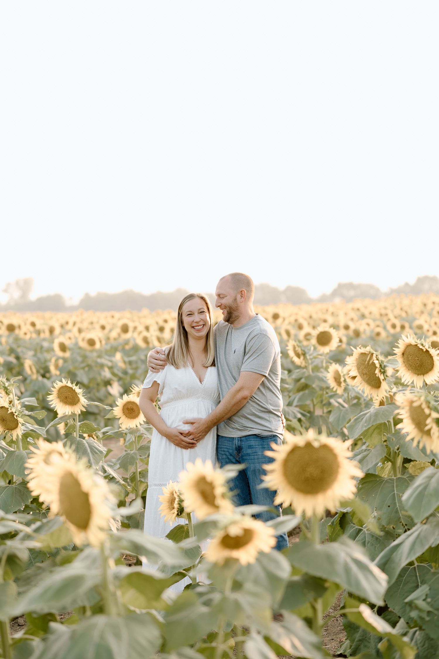 A couple shares a tender moment among blooming sunflowers in a golden field during sunset.