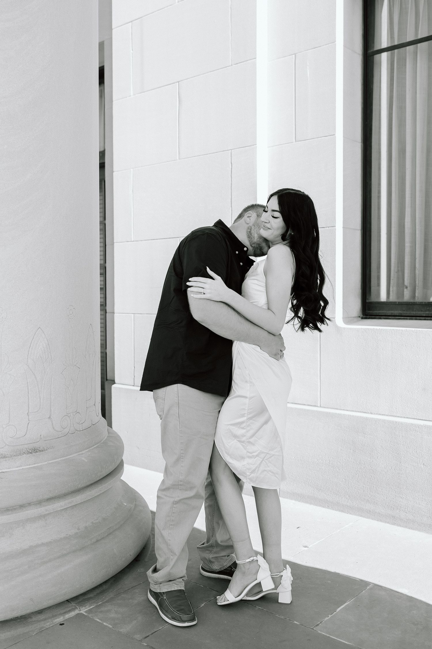 A romantic black and white photo series showing a couple embracing and dipping in front of a classical building column.