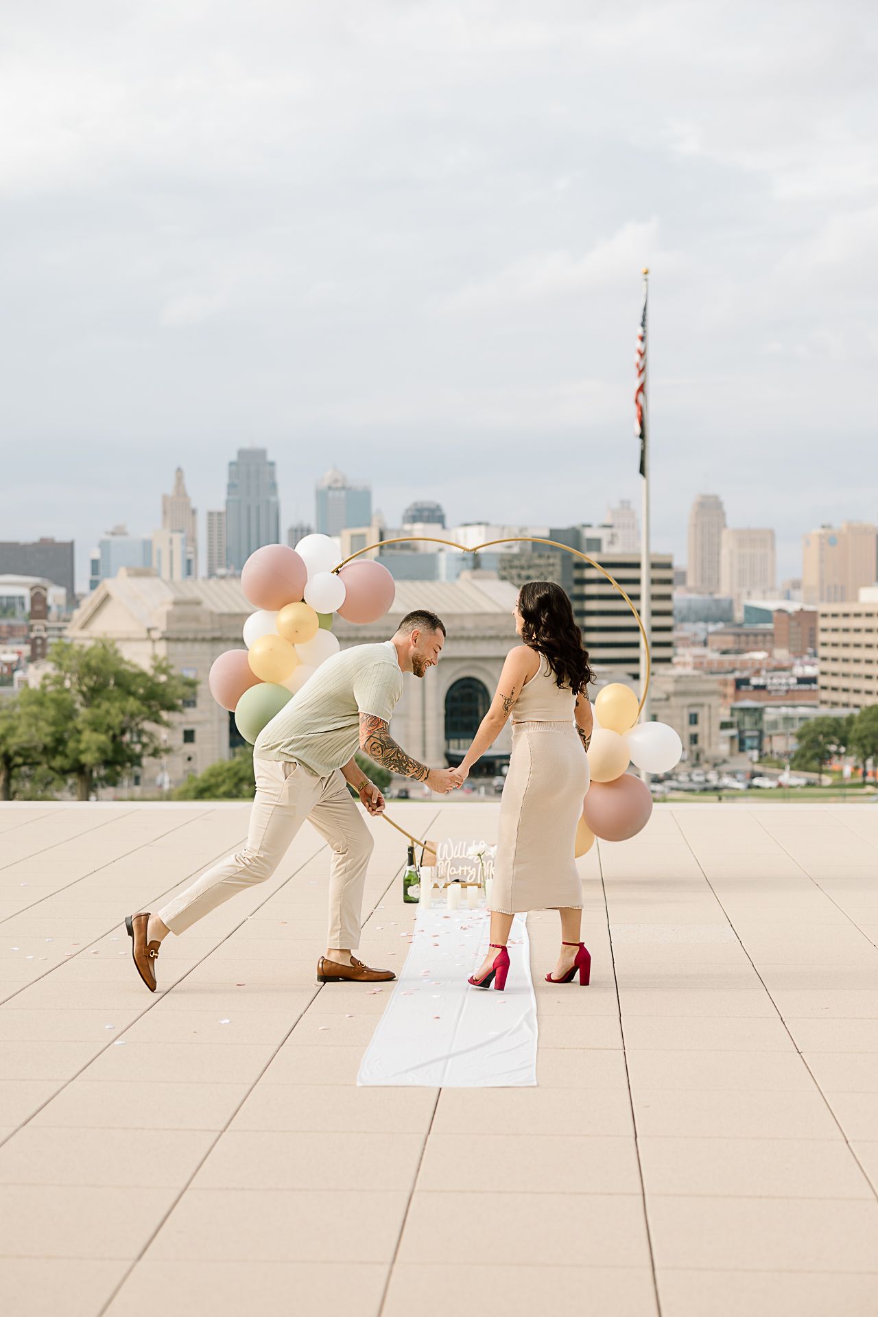 People in light colored outfits playing with balloons on a rooftop with a city skyline backdrop.
