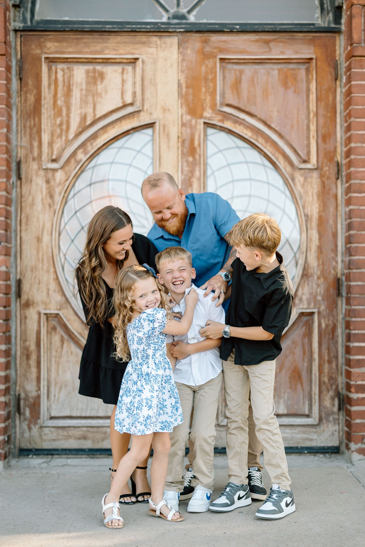 Family sharing laughter and embraces in front of an ornate vintage doorway during a photo session.