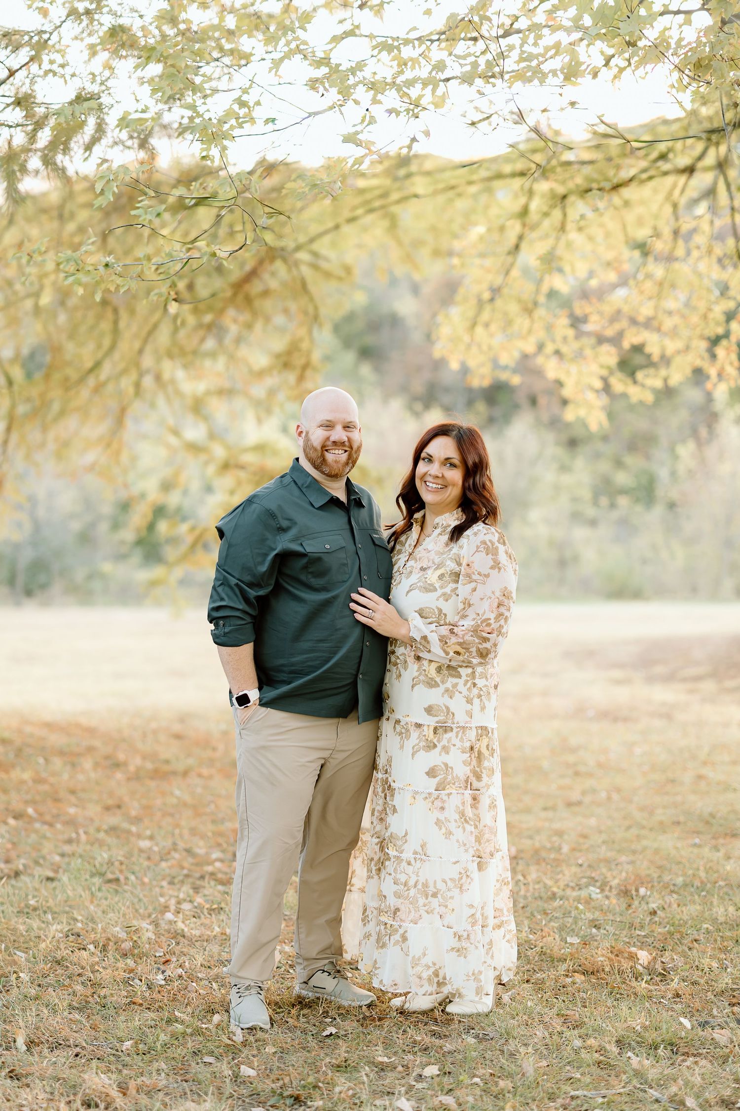 A couple shares tender moments in an autumn setting with golden leaves and soft sunlight filtering through trees.