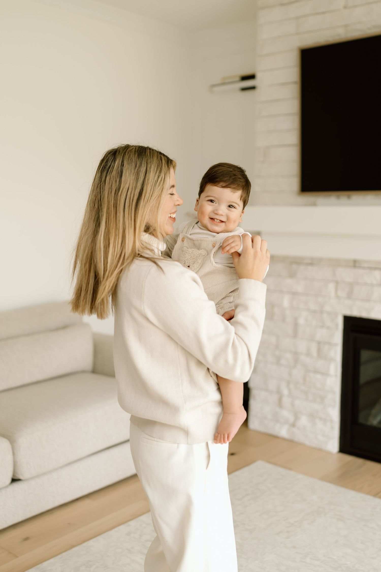 Parent and child share a joyful moment in a bright modern living room with white brick fireplace and hardwood floors.