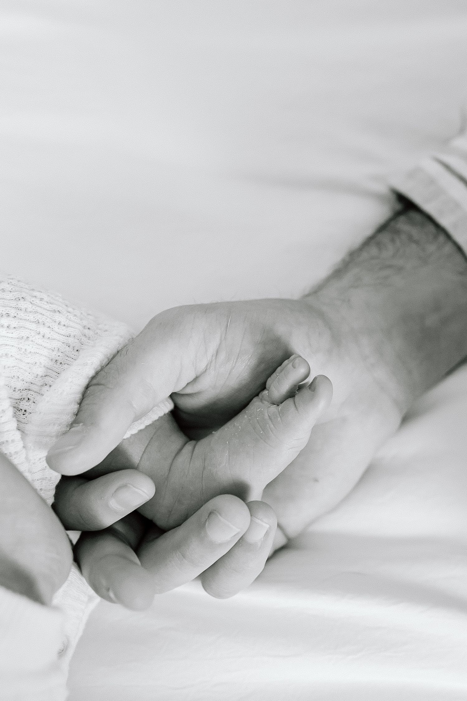 A tender black and white photograph shows two hands gently clasping together against a soft white background.
