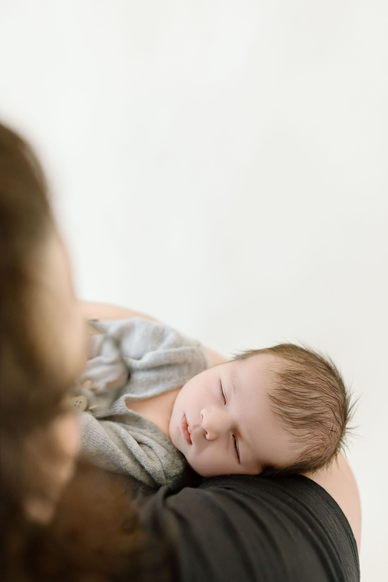 A young child with short brown hair sleeps peacefully on a dark cushioned surface wearing a gray sweater.