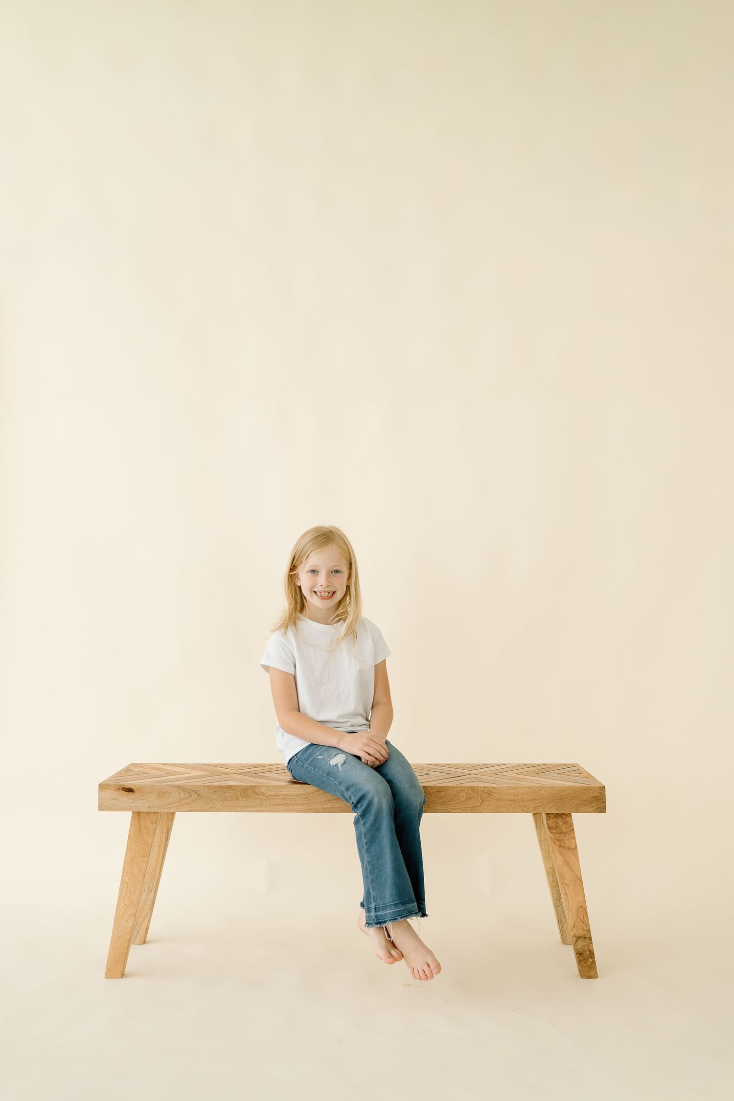 A wooden bench photographed in a minimalist studio setting with neutral background and simple styling.