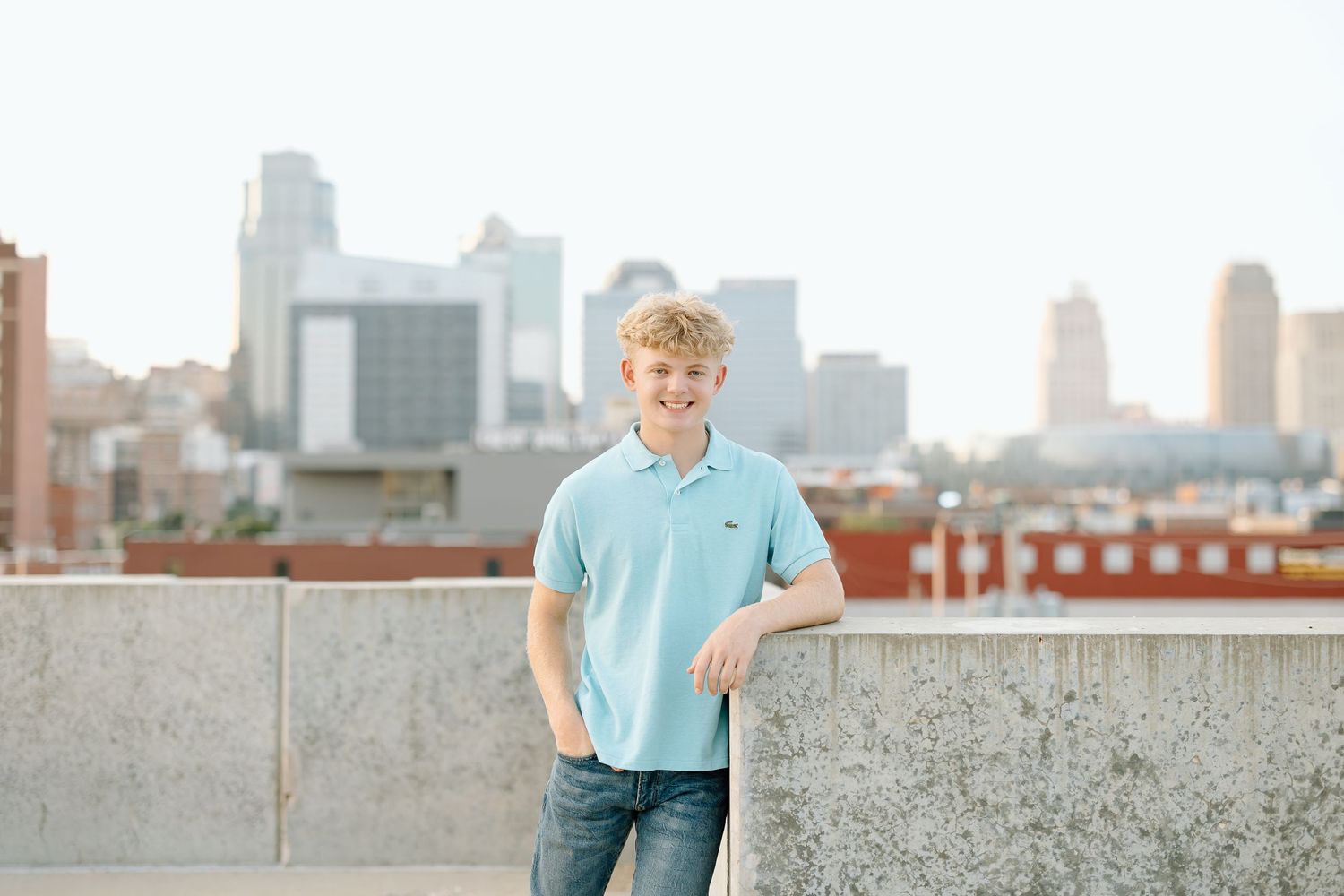 A person in a light blue shirt poses against a city skyline backdrop on a rooftop terrace.