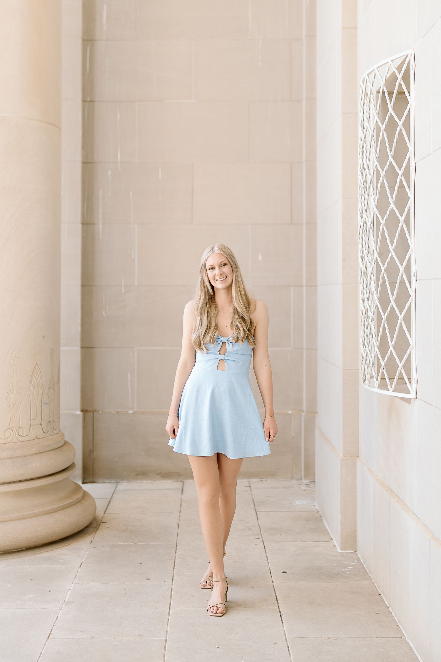 A woman in a light blue dress walks through an elegant colonnade with white pillars and latticed windows.