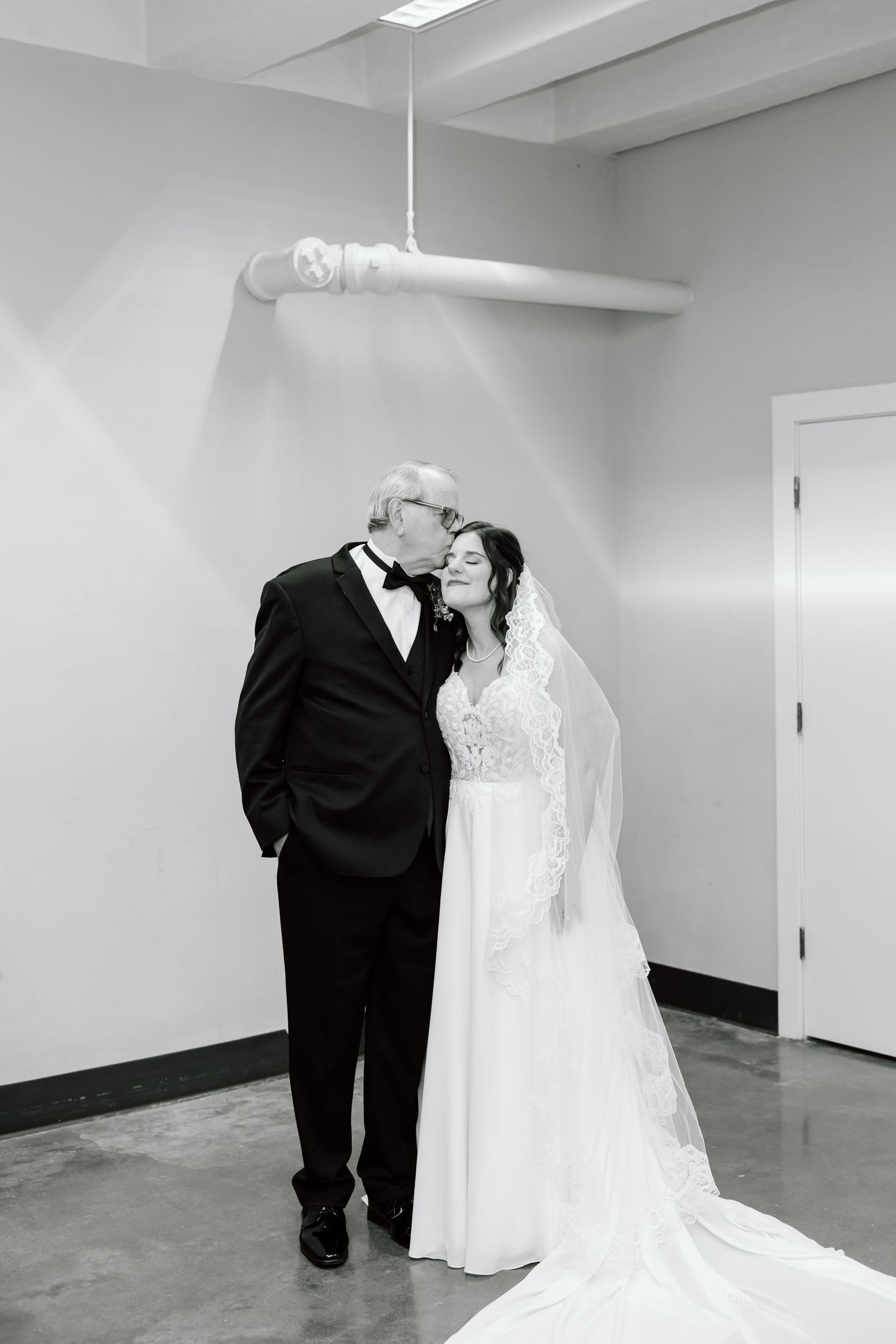 A bride and groom share an intimate moment in a minimalist white hallway during their wedding day.