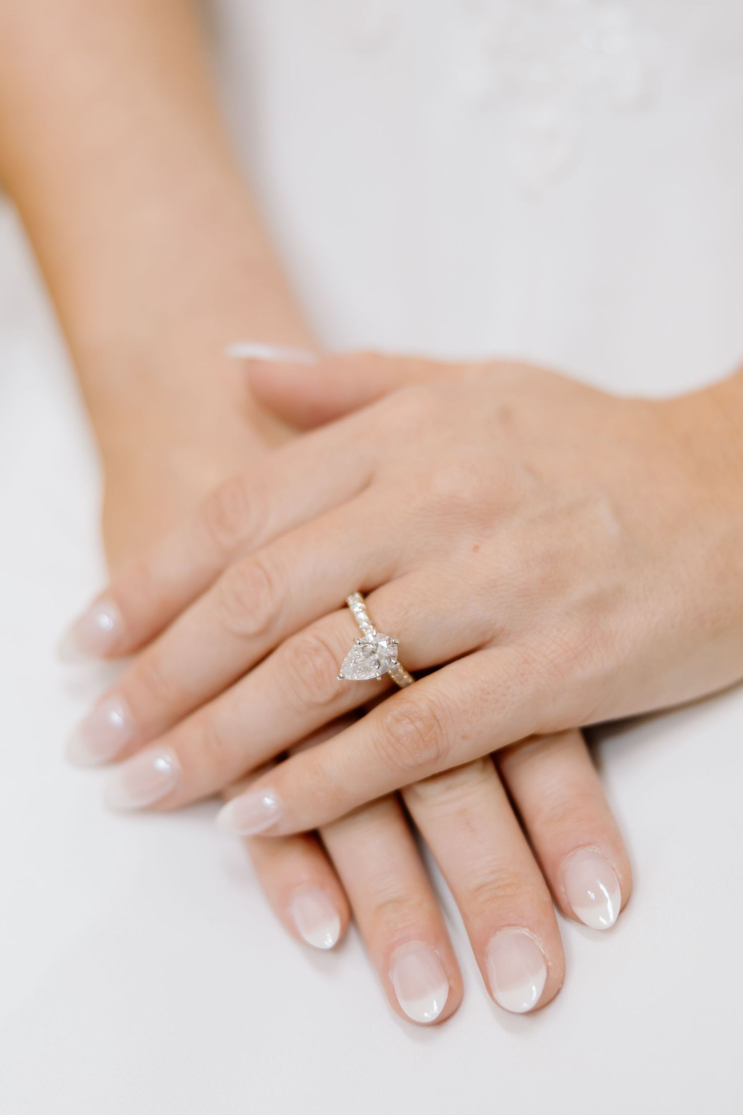 Close-up of manicured hands with French tips and a sparkling diamond solitaire engagement ring on white background.