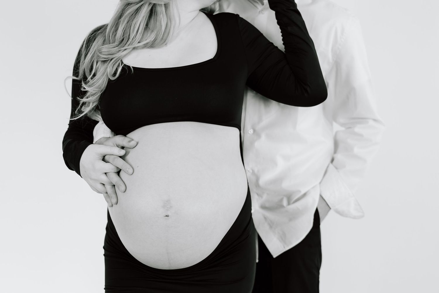 Close-up black and white shot of a pregnant woman's belly as her partner holds her.