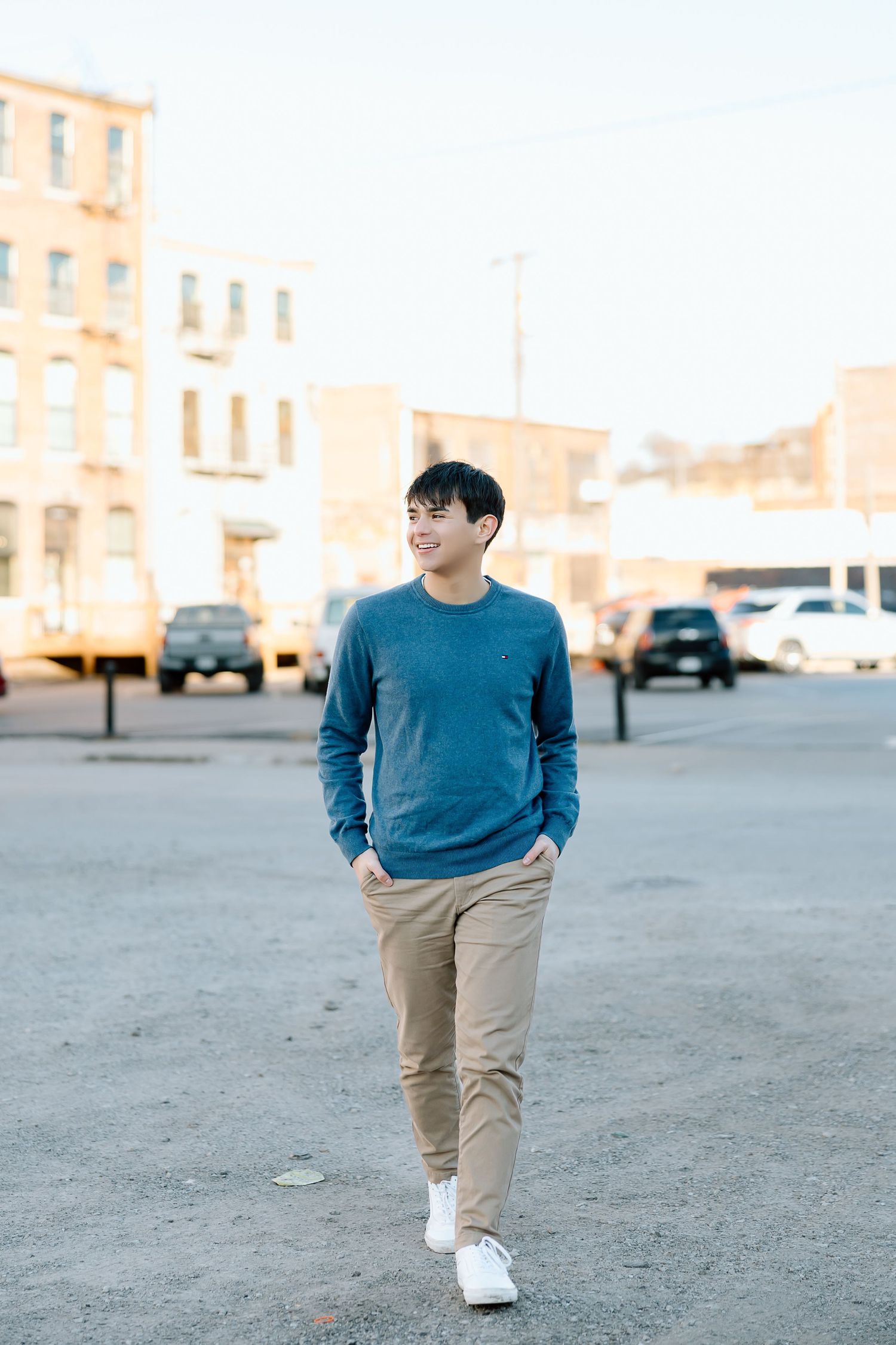 Stylish casual portrait of person in blue sweater walking through urban setting with buildings.