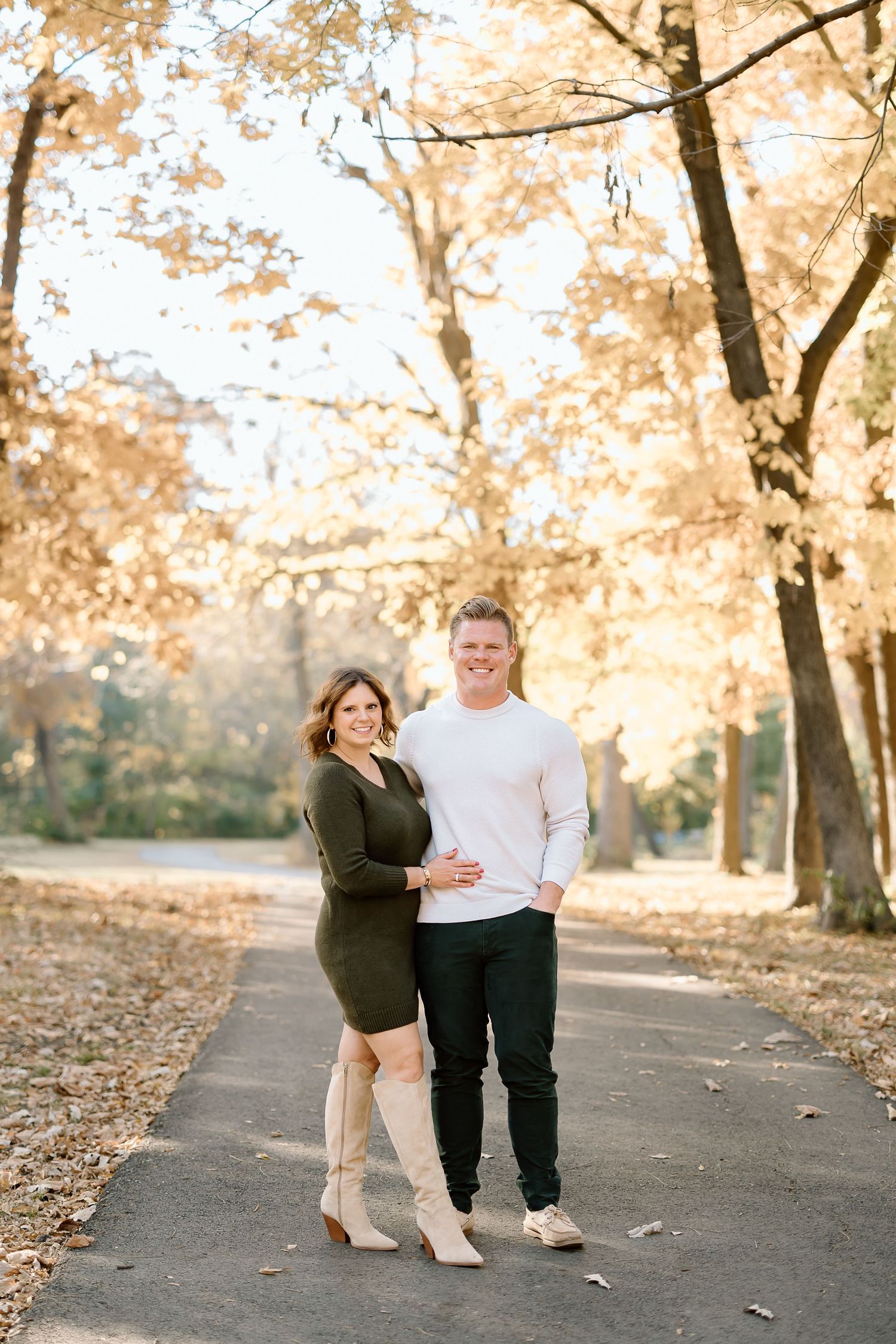A couple poses together on a path with golden autumn foliage in the background.