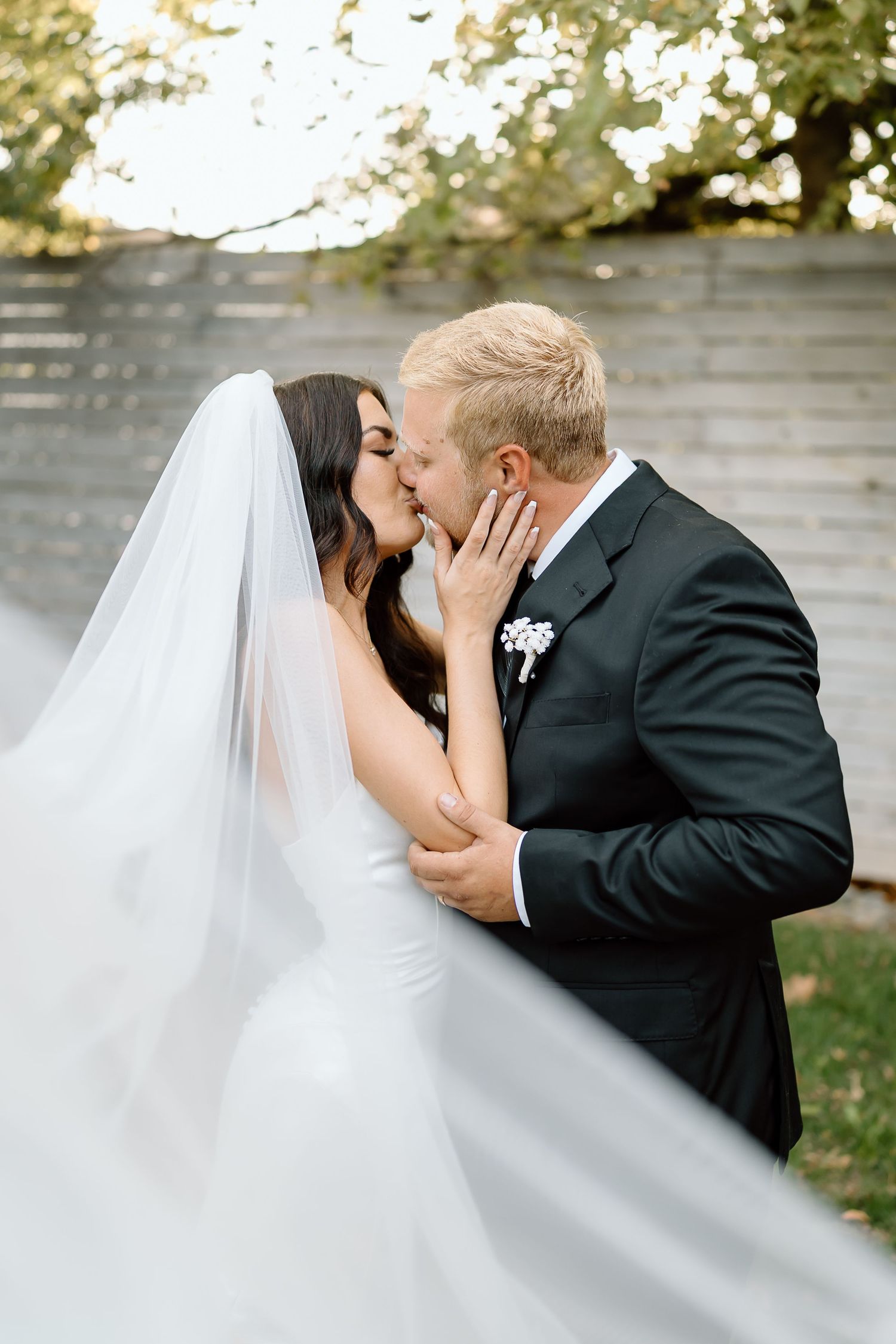 A bride and groom share a passionate kiss during their outdoor wedding ceremony.