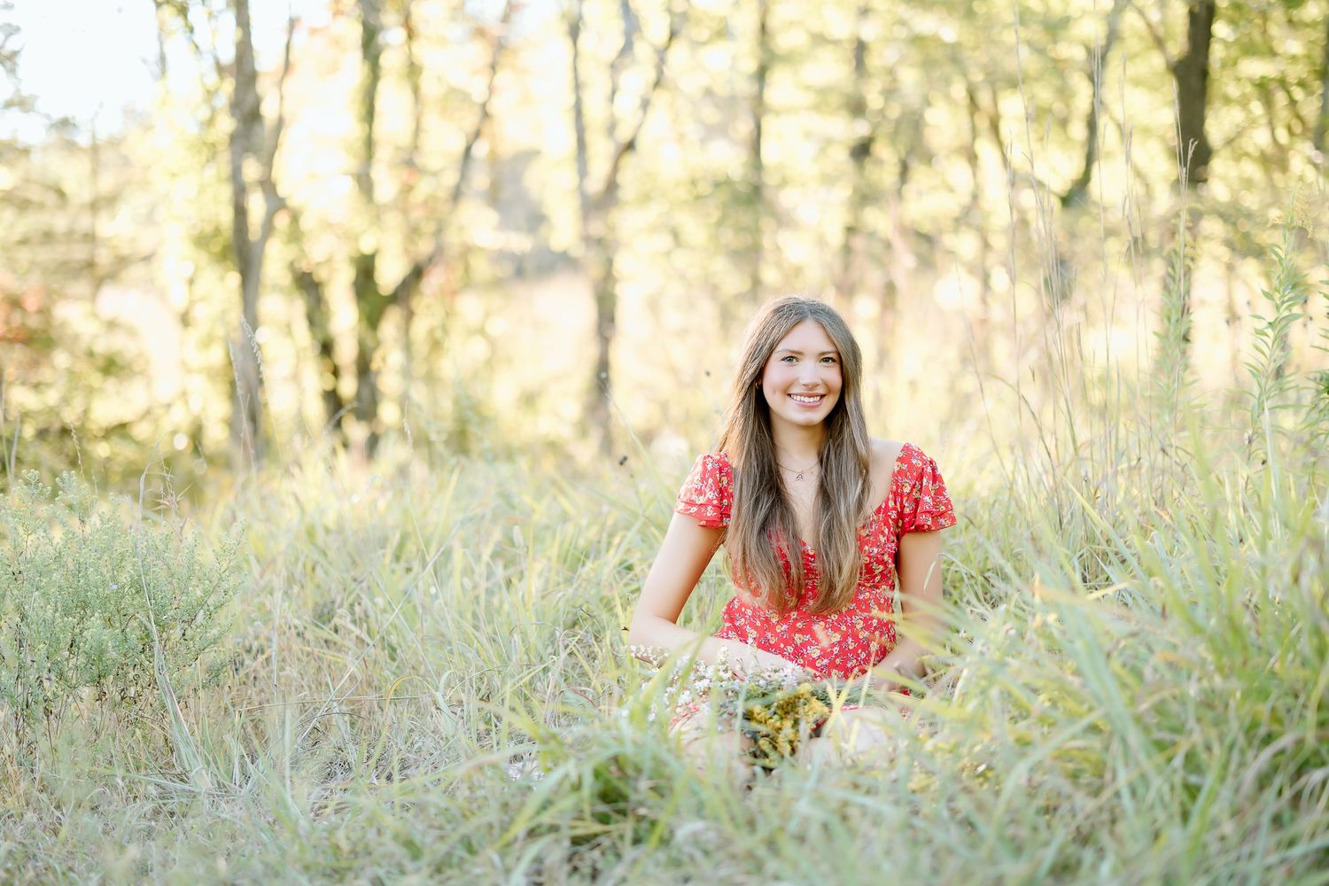 A person in a bright red sweater stands in a sunlit meadow of tall grass during golden hour.