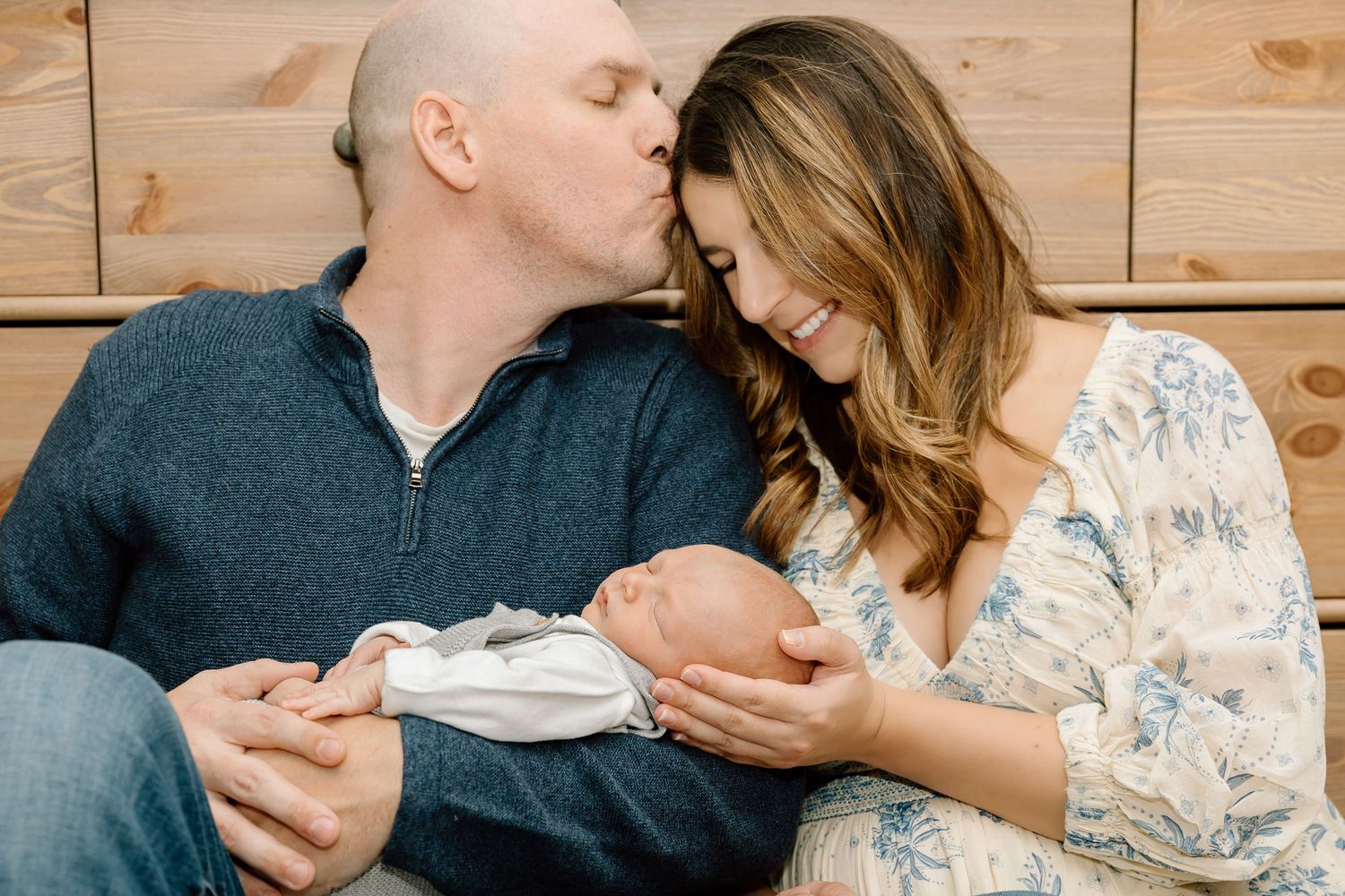A couple sitting together holding tiny baby shoes while sharing an intimate moment on a wooden background.