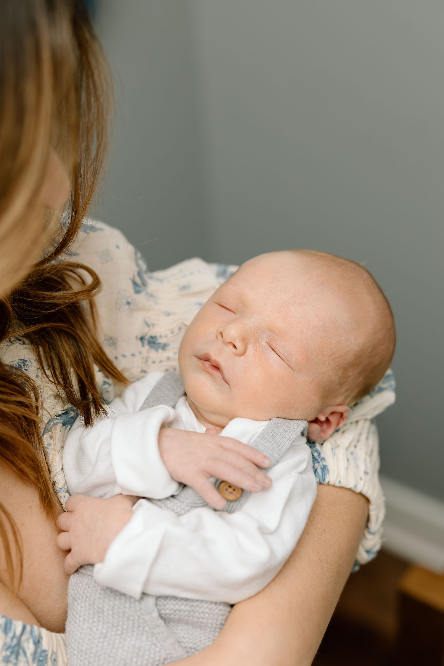 A sleeping newborn baby in white clothing rests peacefully in someone's arms.