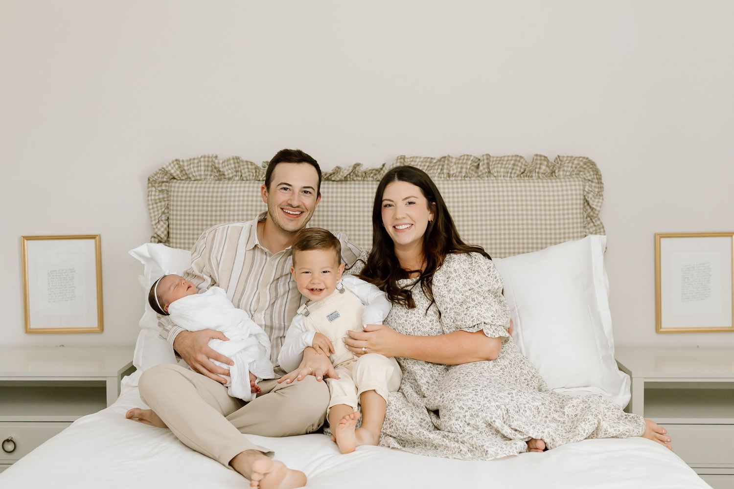 Family relaxing together on white bedding in a bright bedroom with neutral decor and framed artwork.