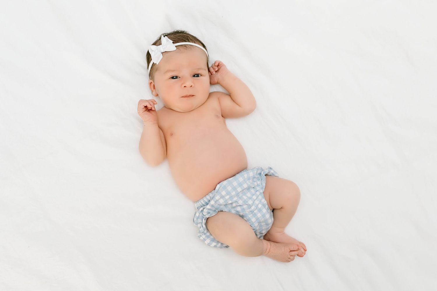 Baby wearing a light blue headband lying on white fabric in a gentle sleeping pose.