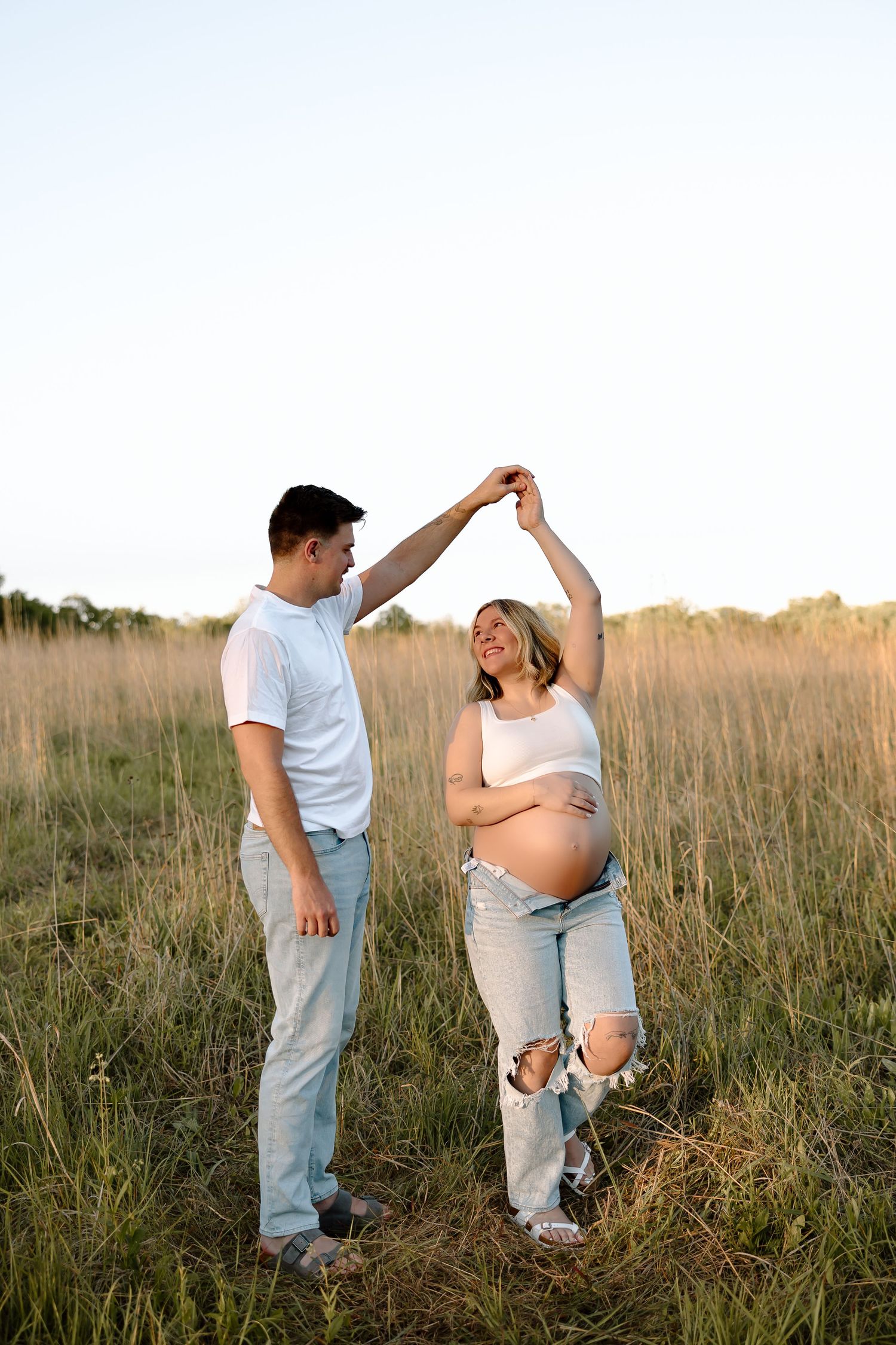 A couple stands together in a golden field during sunset while sharing an intimate moment.