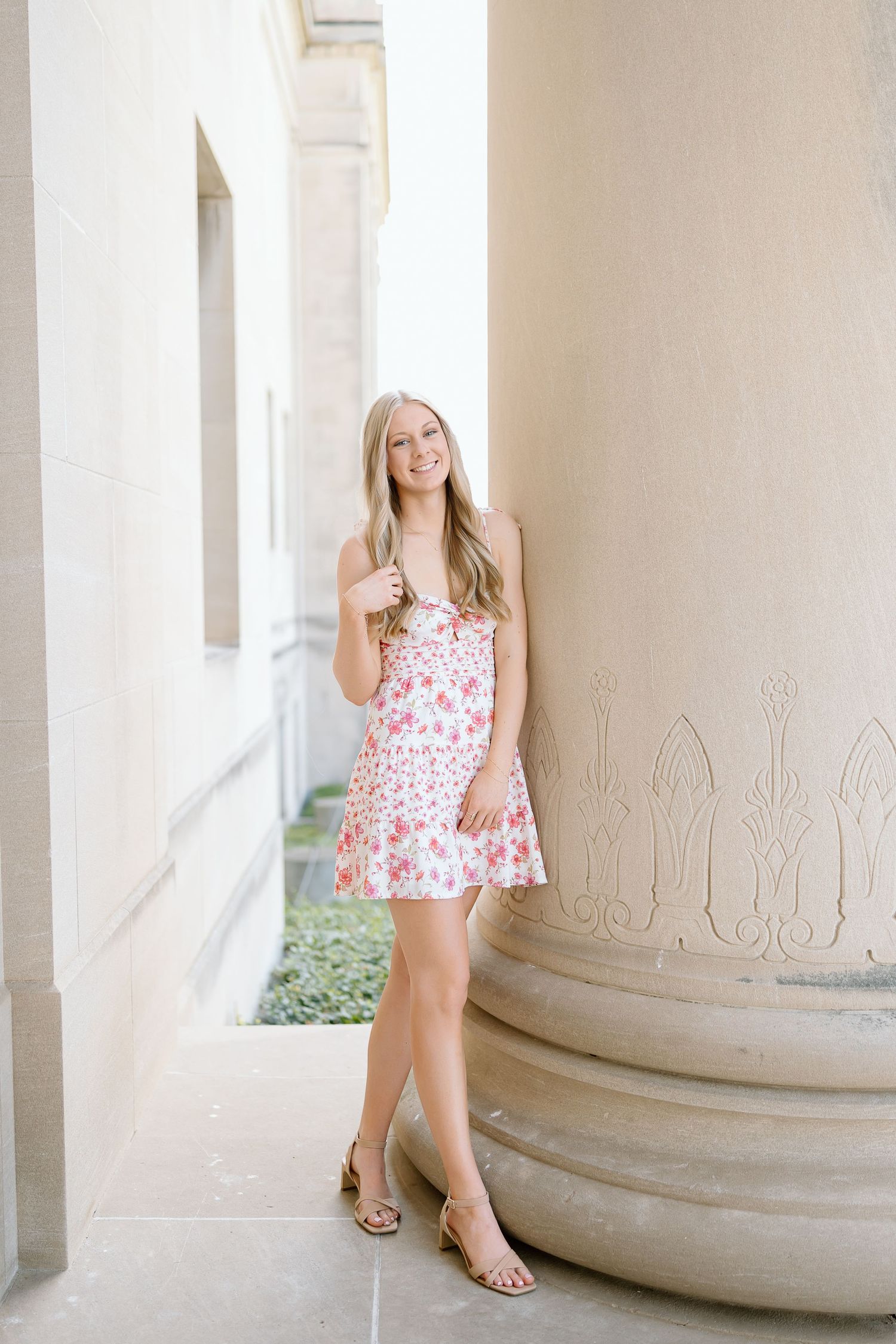 A floral print summer dress is showcased against classic white stone columns in an elegant architectural setting.
