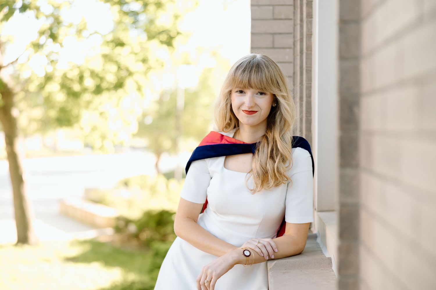 A person in a white dress with red and navy color blocking sits outdoors in natural sunlight.