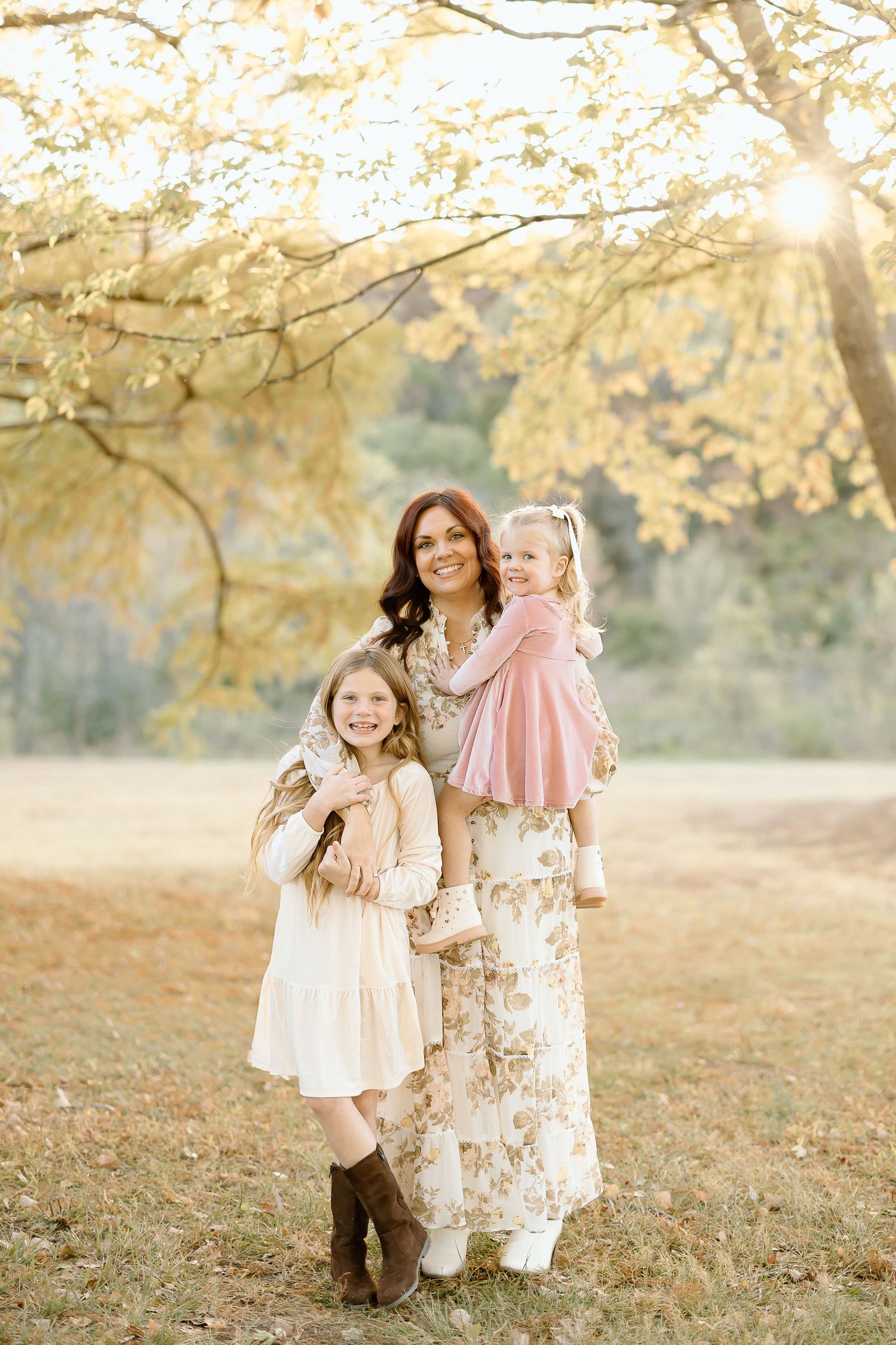 Three young children play and laugh together under golden autumn trees during a sunset photo session.