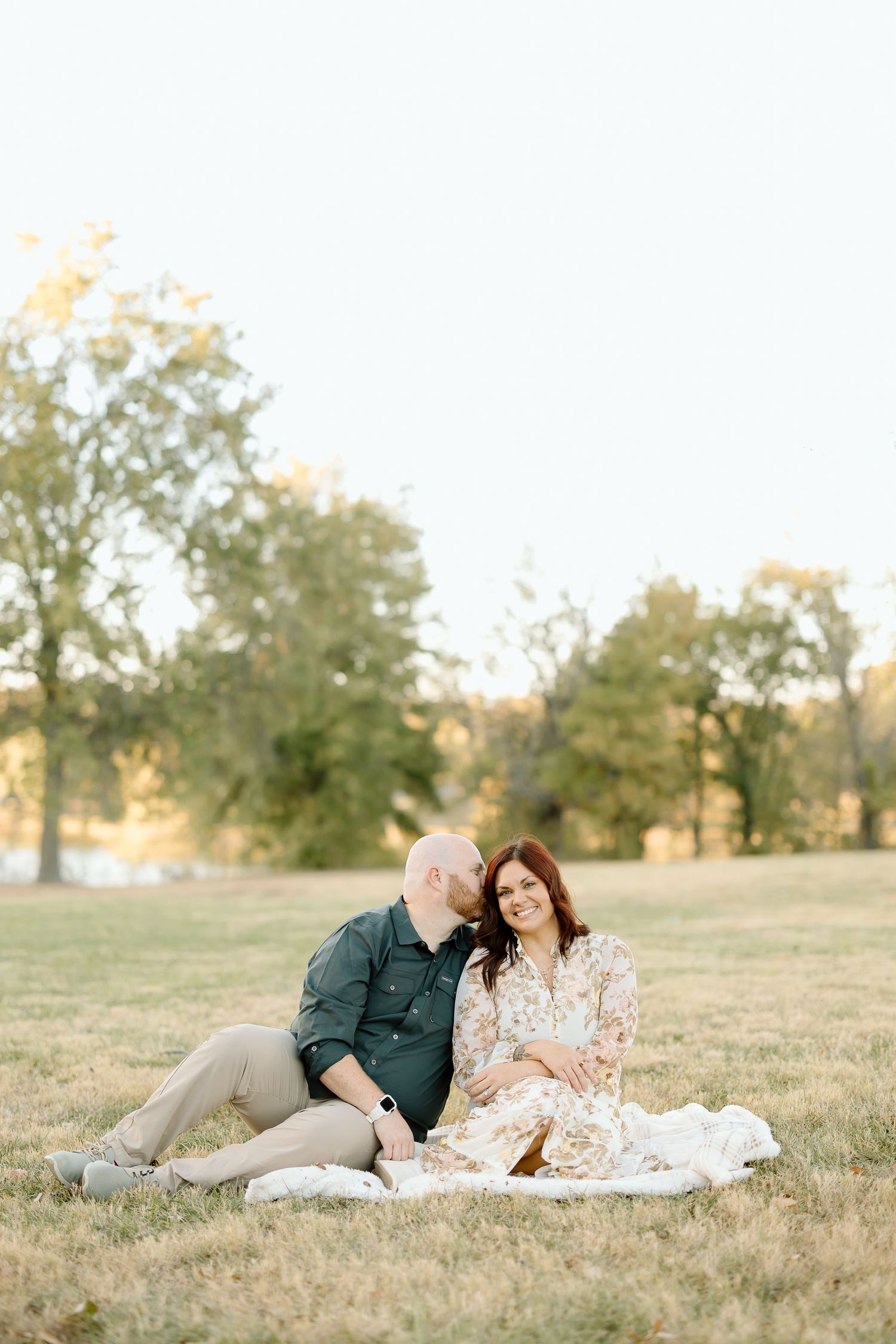 A couple relaxes together on a white blanket in a sunlit grassy field during golden hour.