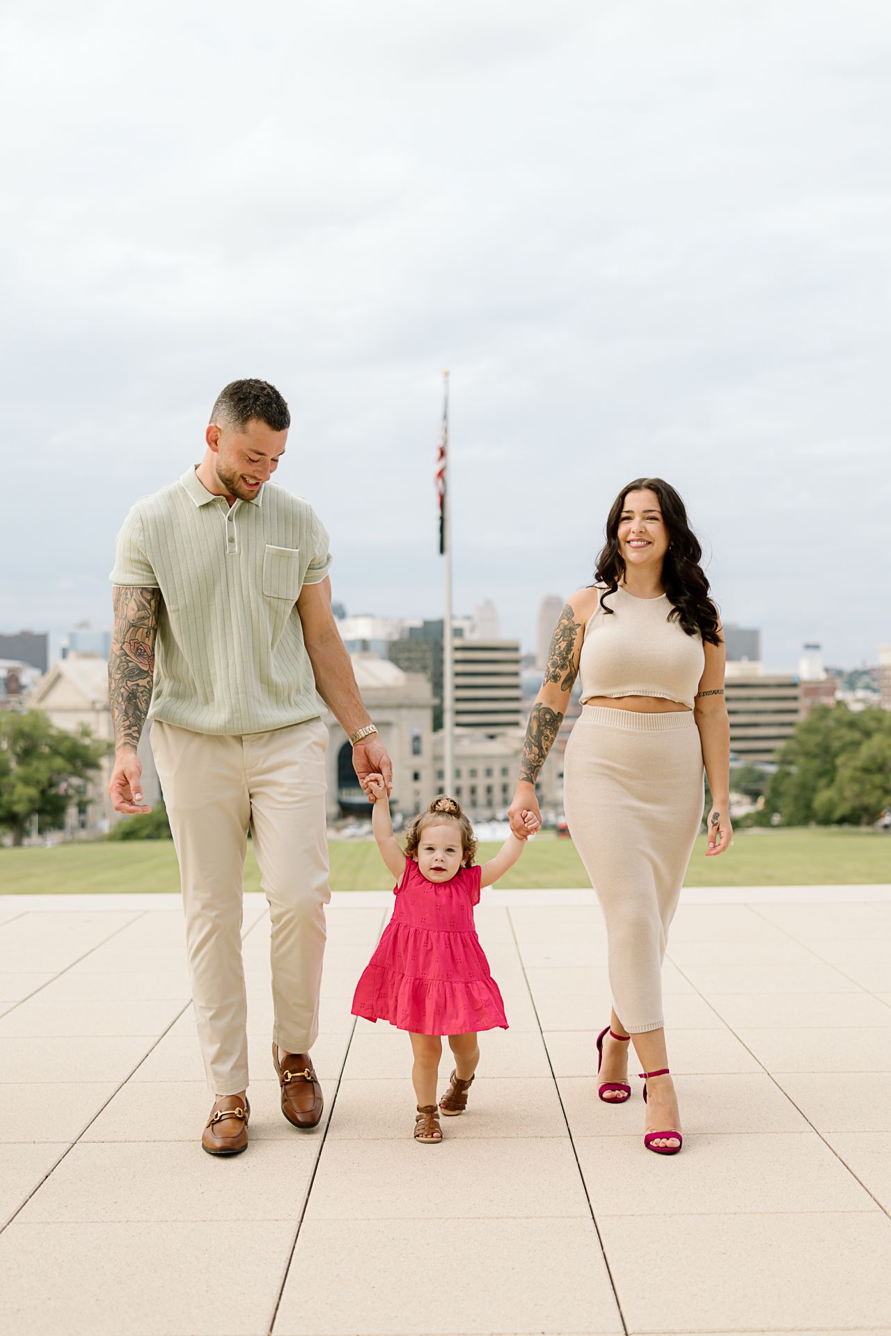 A family walking and playing together on a concrete plaza while wearing coordinated neutral-toned outfits.