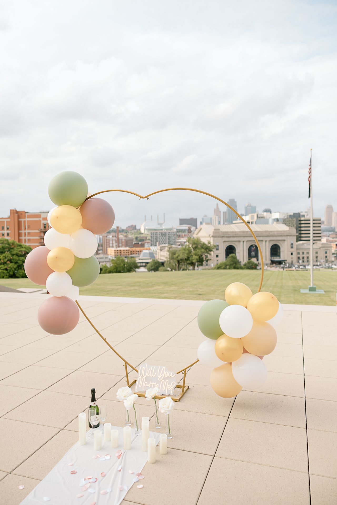 Elegant pastel balloon arch installation with neutral colors against an urban backdrop on a concrete plaza.
