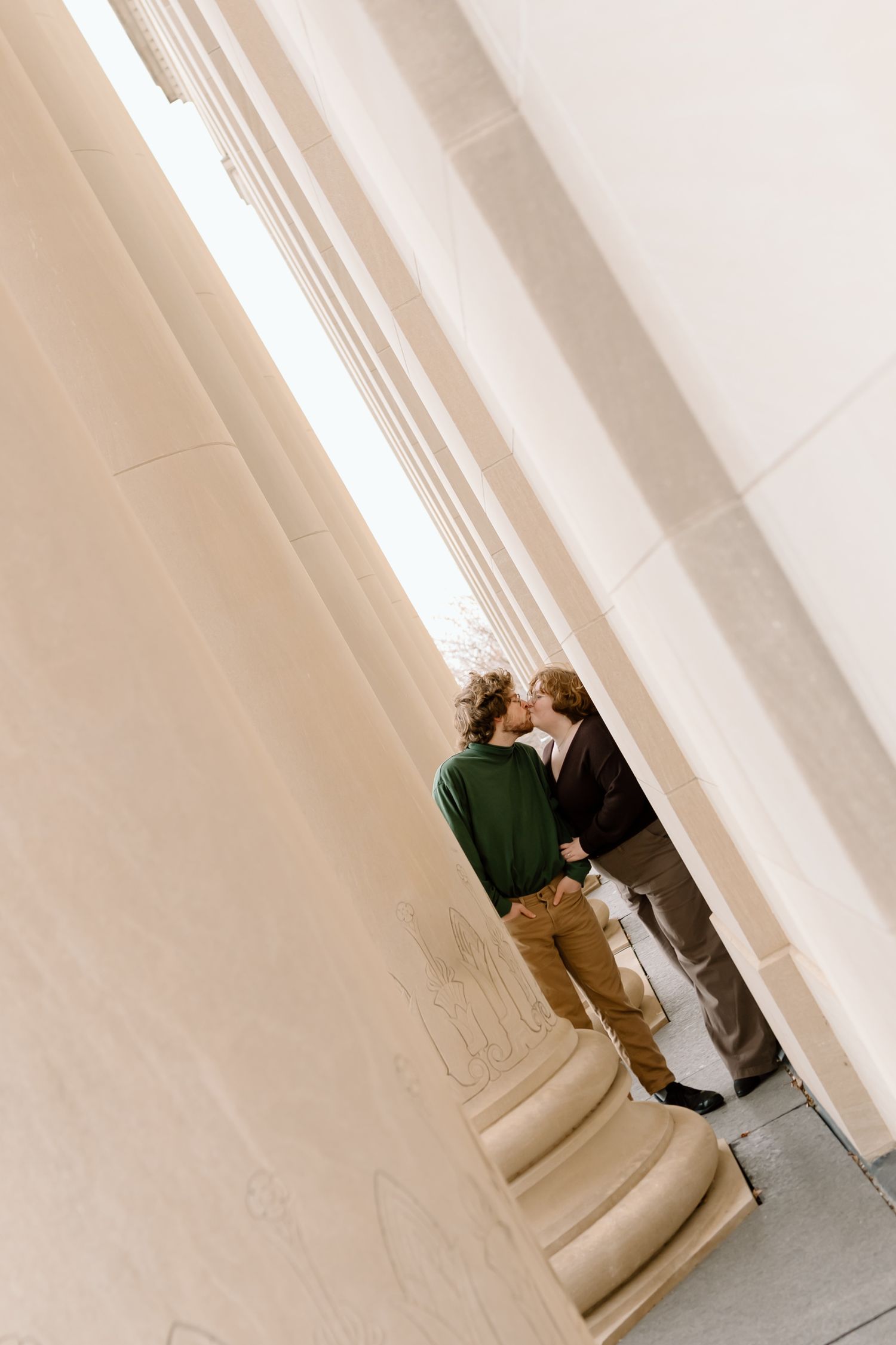 Two people embracing between classical white columns in an architectural setting.