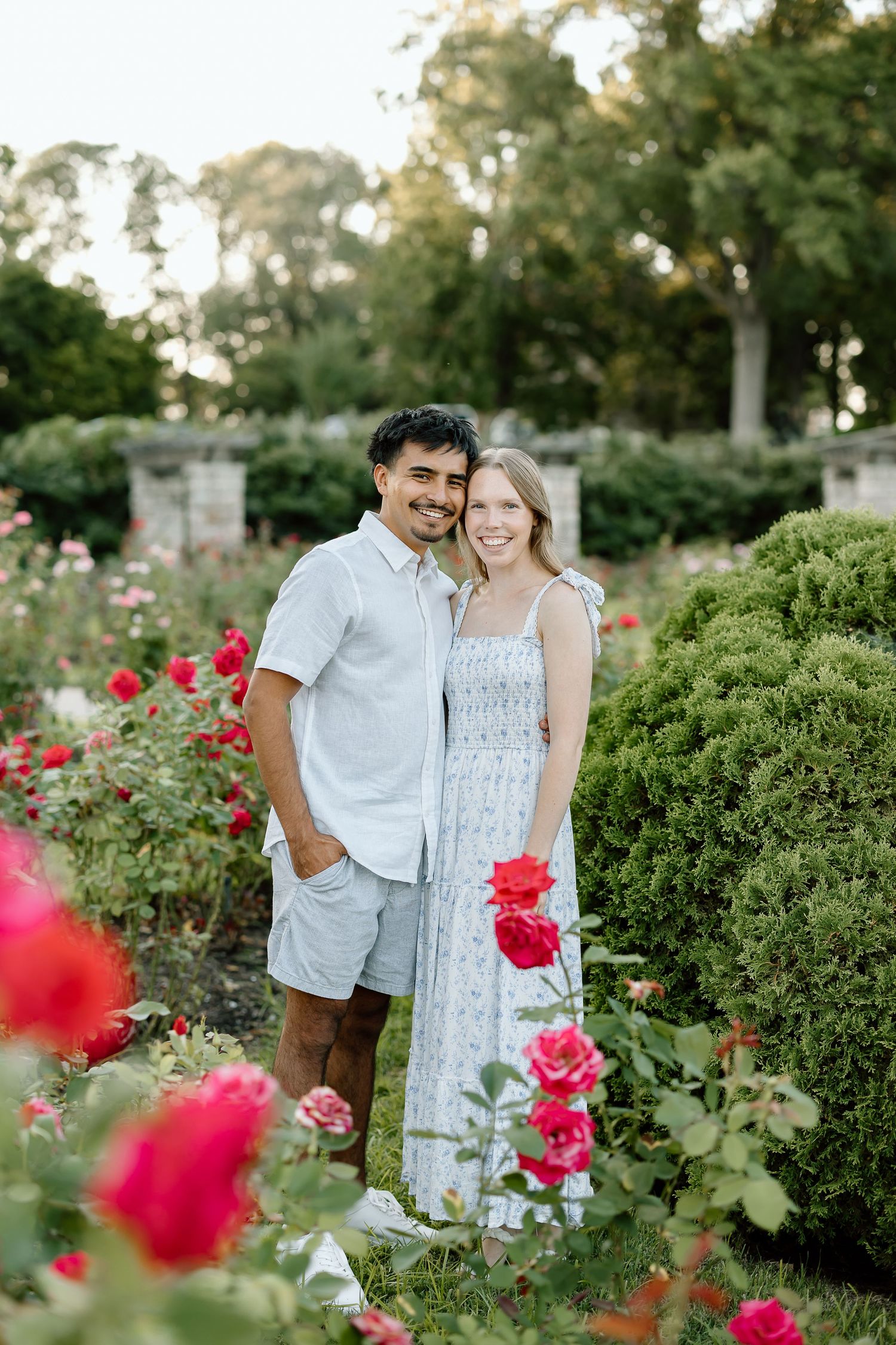 A couple shares a tender moment among blooming rose bushes in a lush garden setting during golden hour.