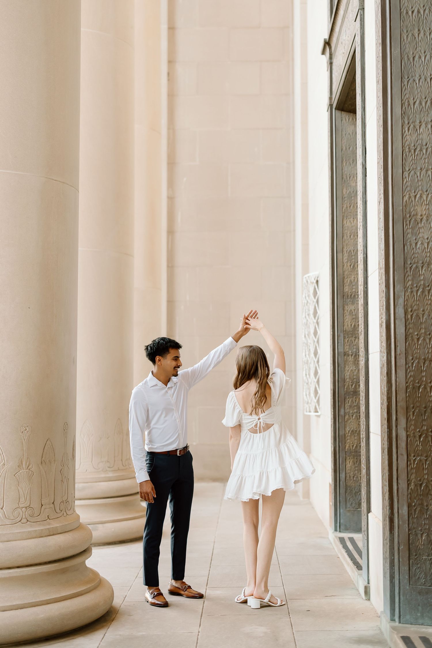 Couple dancing together in an elegant white columned hallway with natural light streaming in through windows.