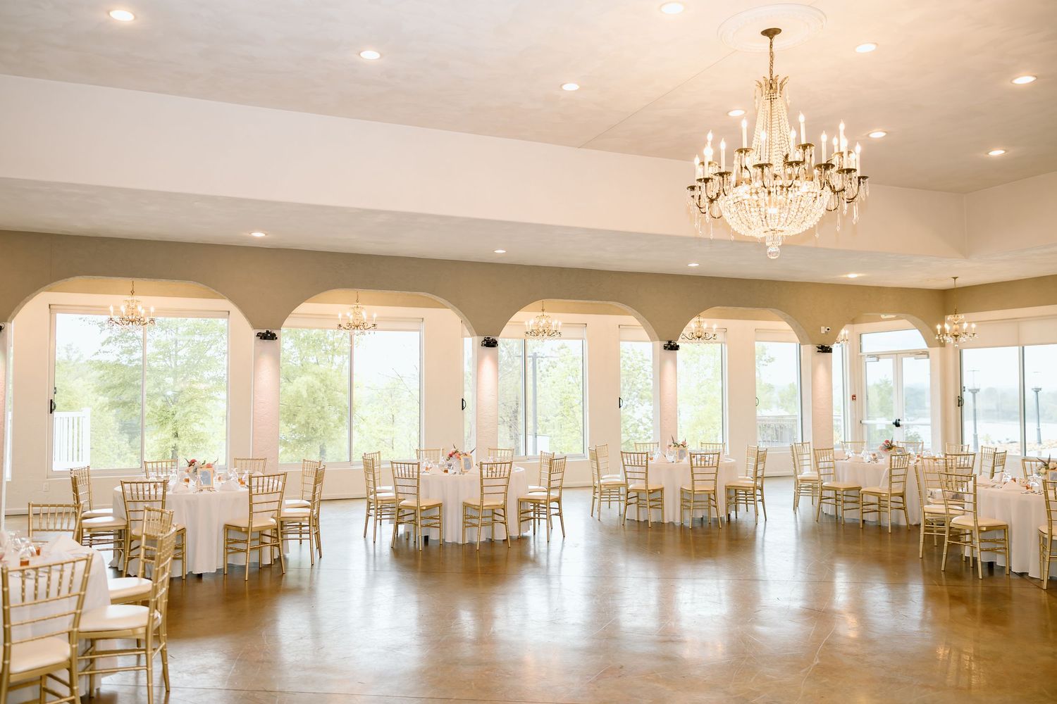 Panoramic view of an elegant white ballroom with crystal chandeliers, large windows, and hardwood floors.
