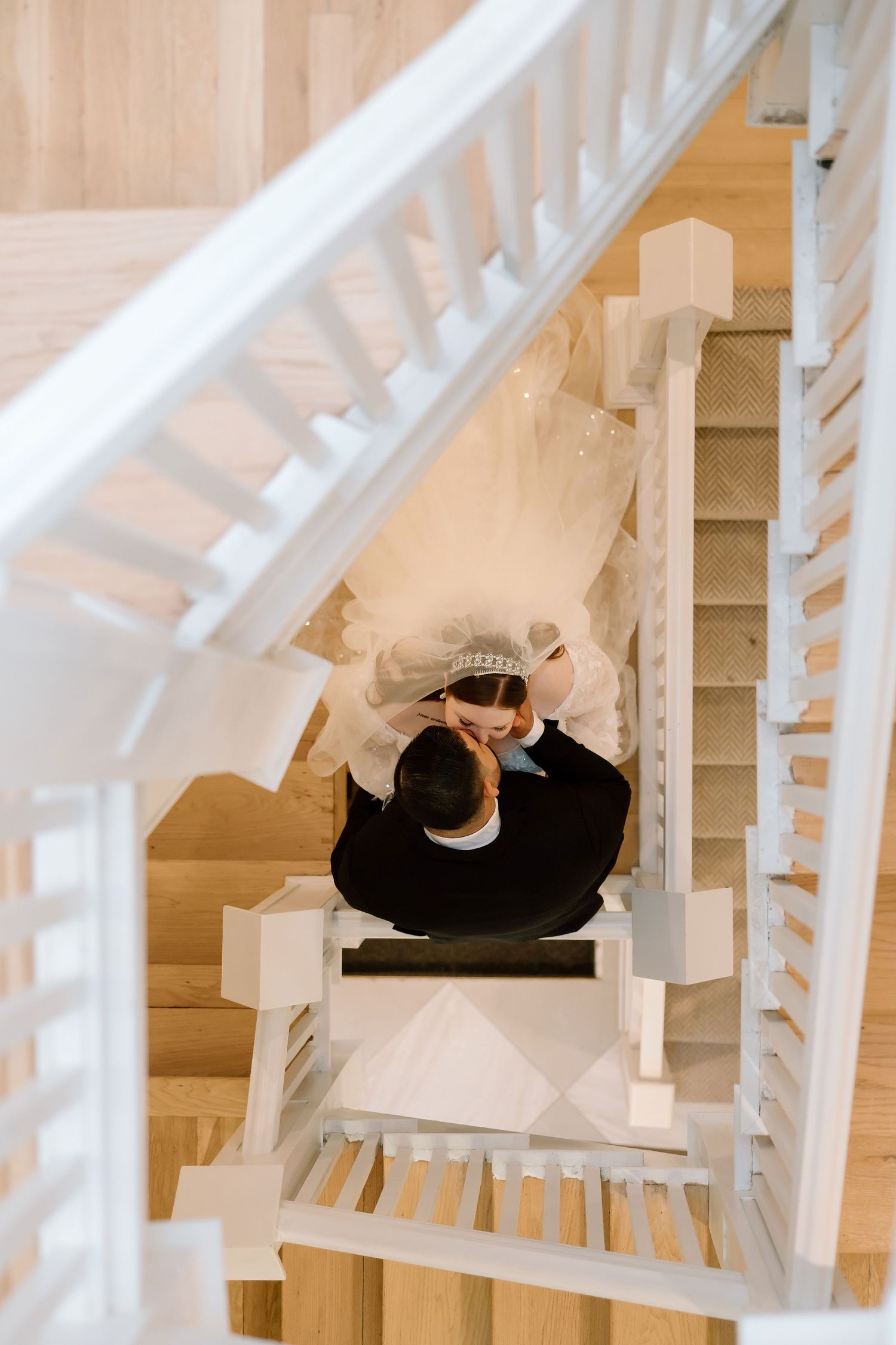 Aerial view of a bride and groom sharing a romantic moment on wooden stairs with white railings.