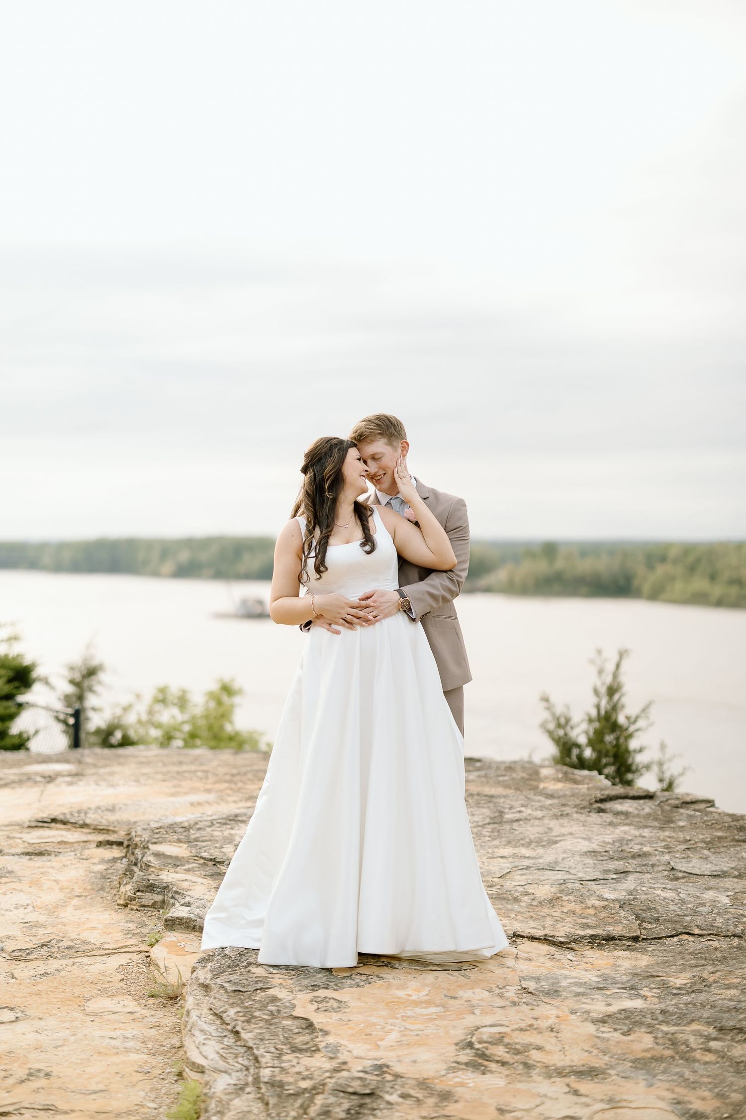 A romantic couple embracing on rocky cliffs overlooking a serene lake.
