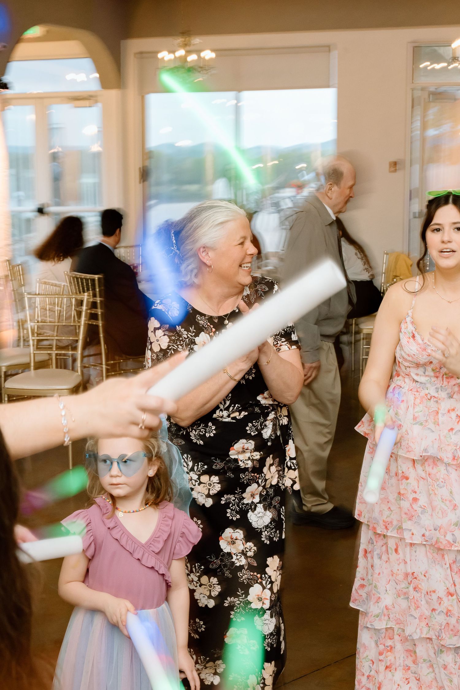 Guests dancing and celebrating at a wedding reception with colorful lights illuminating the dance floor.