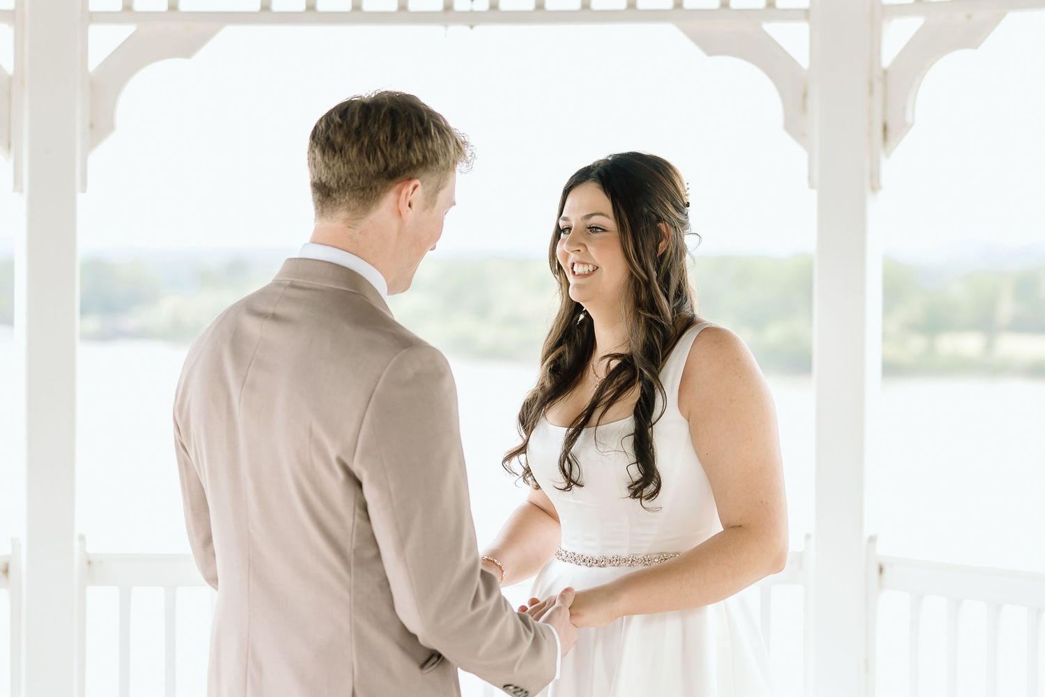 A couple shares a tender moment during their wedding ceremony on a bright white gazebo overlooking scenic views.