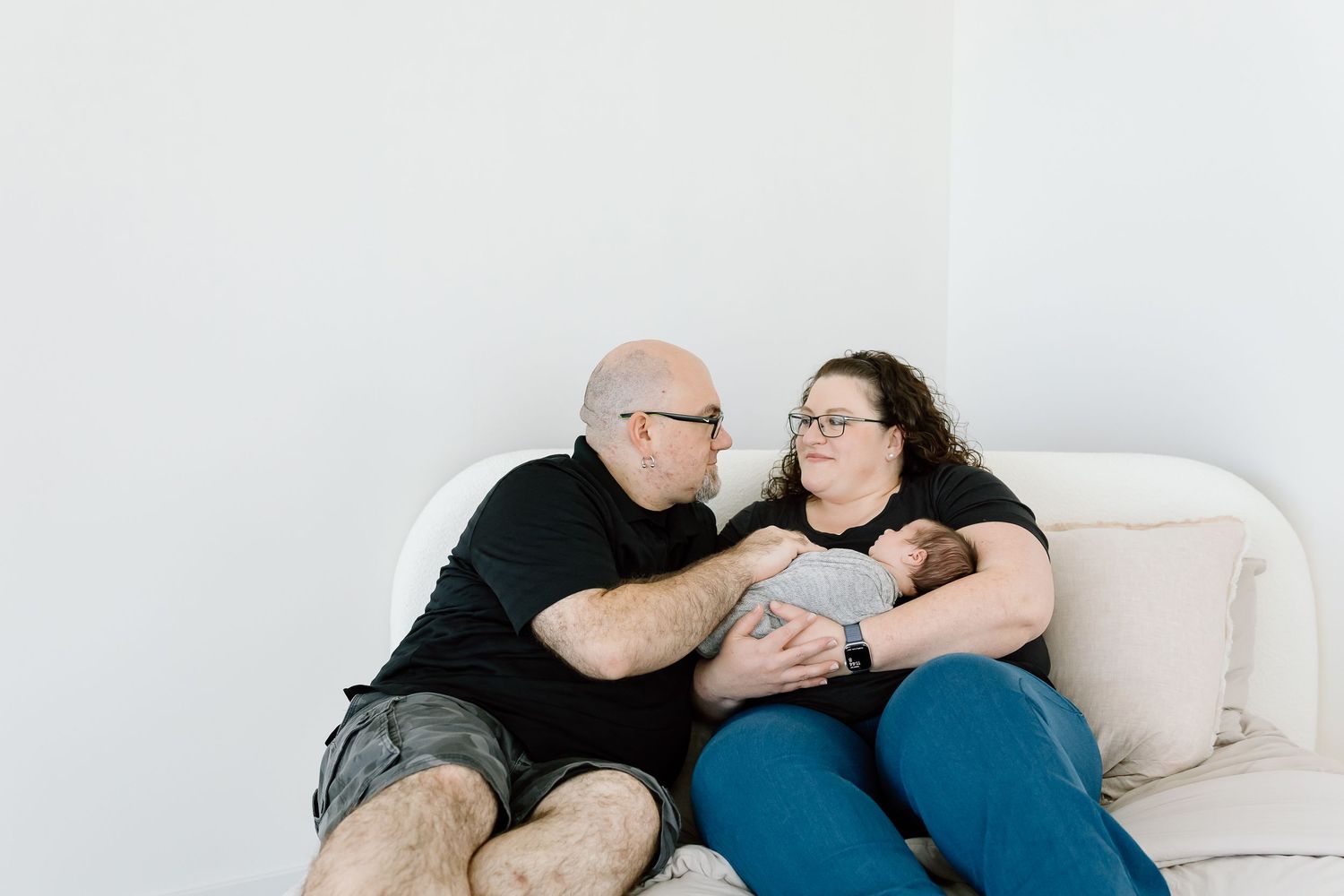 A couple lies together on a white couch in a loving embrace.