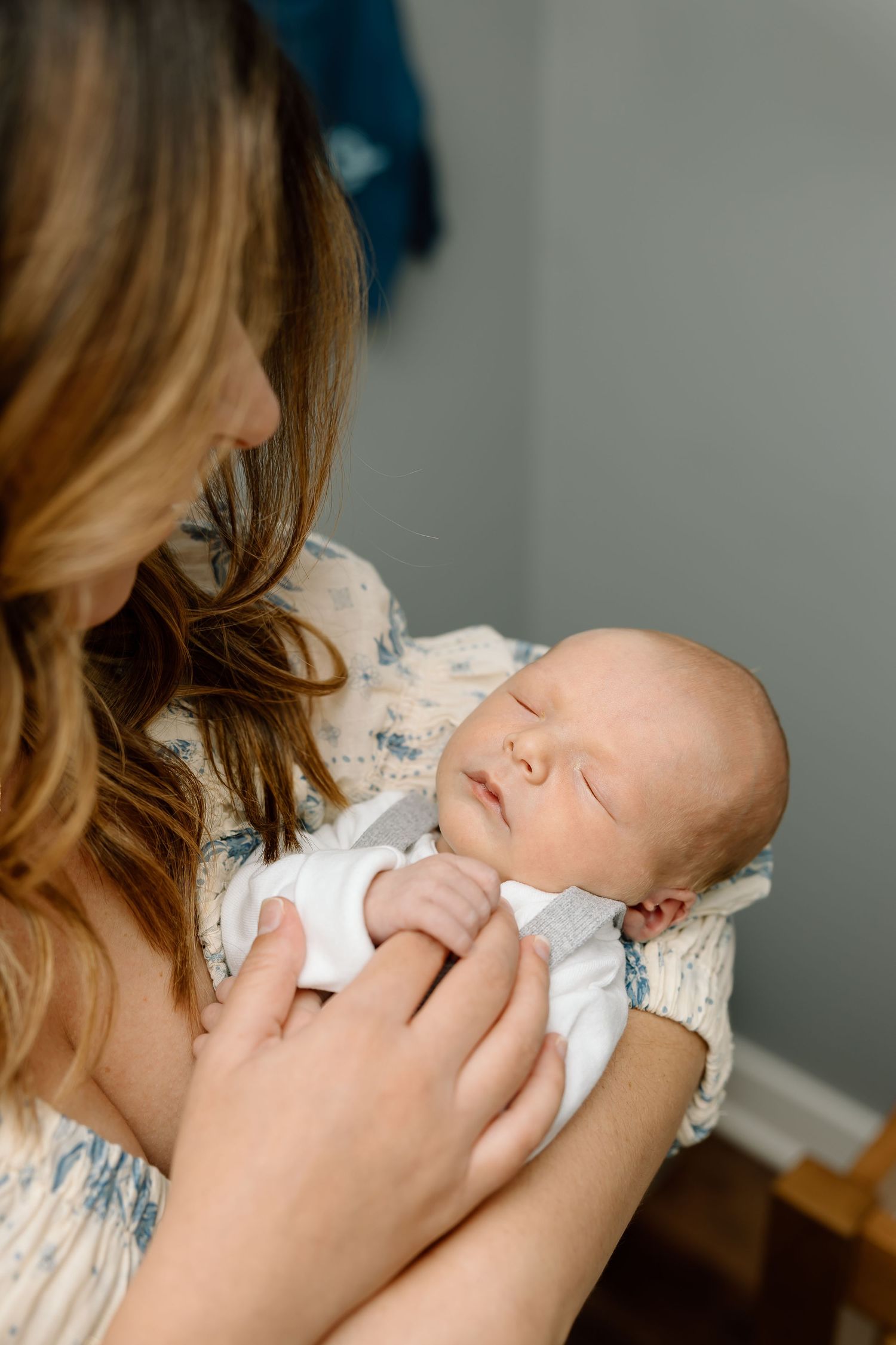 A sleeping newborn baby in white lace clothing is gently cradled in a caregiver's arms.