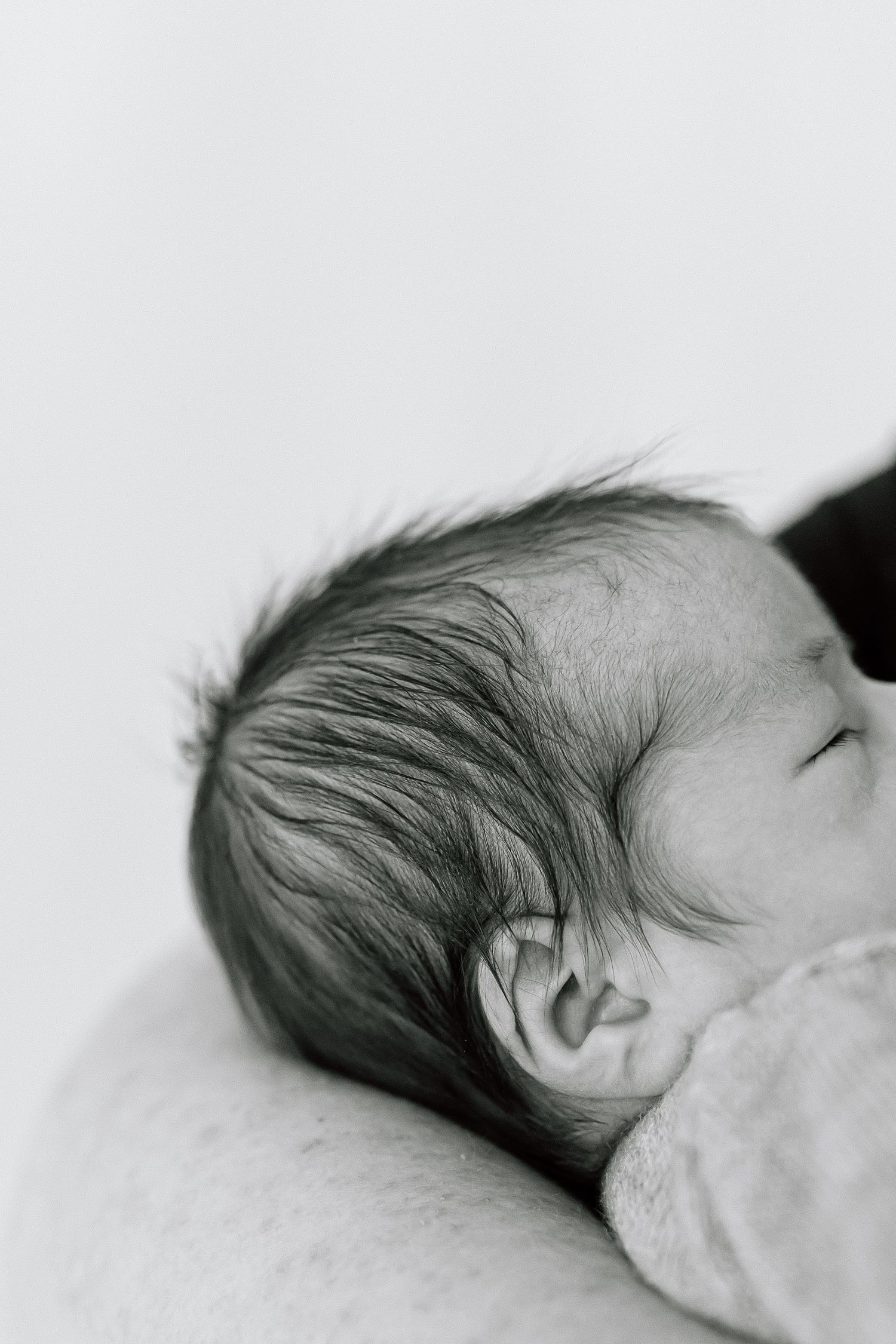 Black and white close-up of a sleeping baby's head resting on a soft surface.