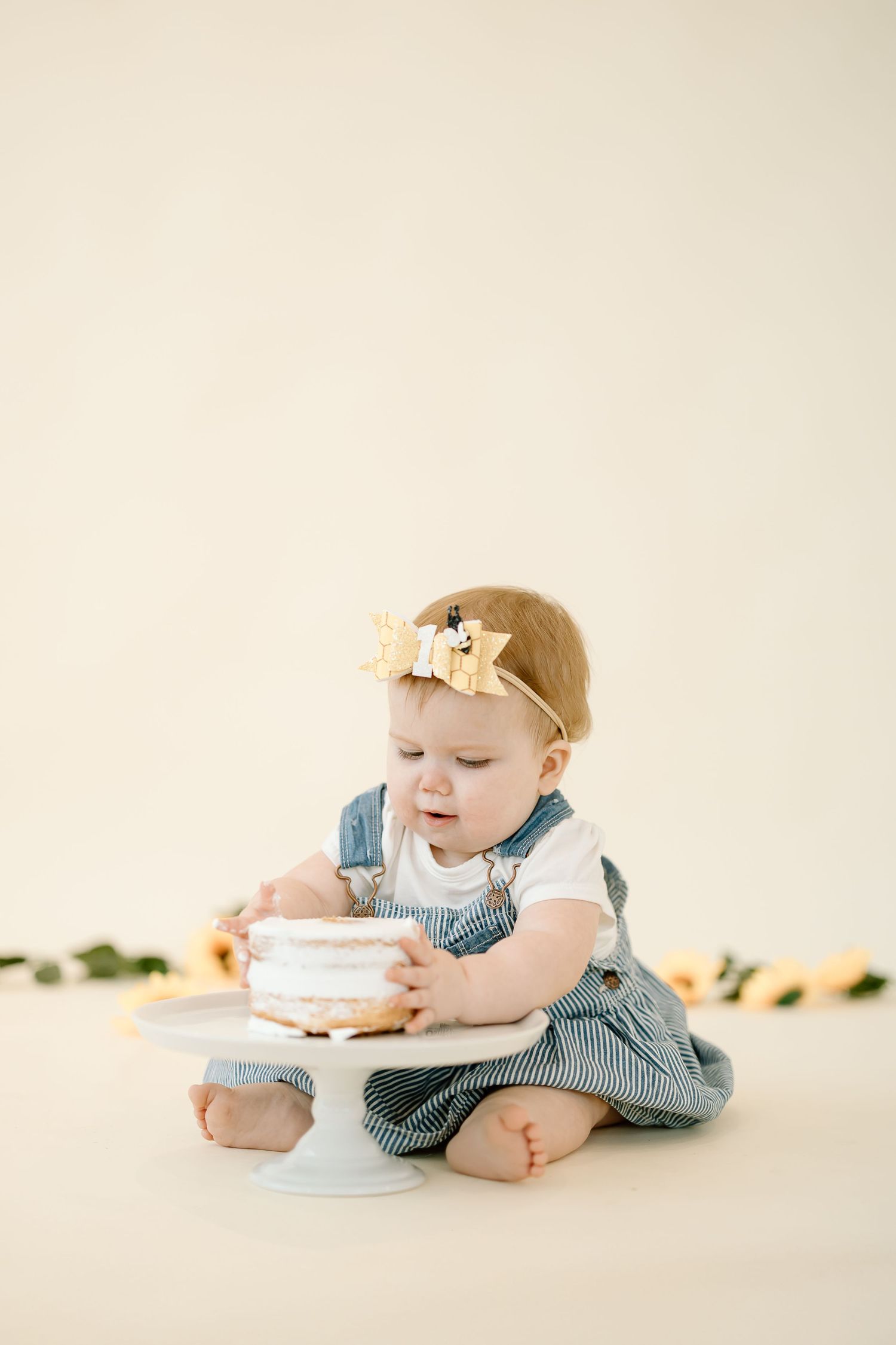 Baby in gingham romper crawls and plays with cake during first birthday cake smash photo session.