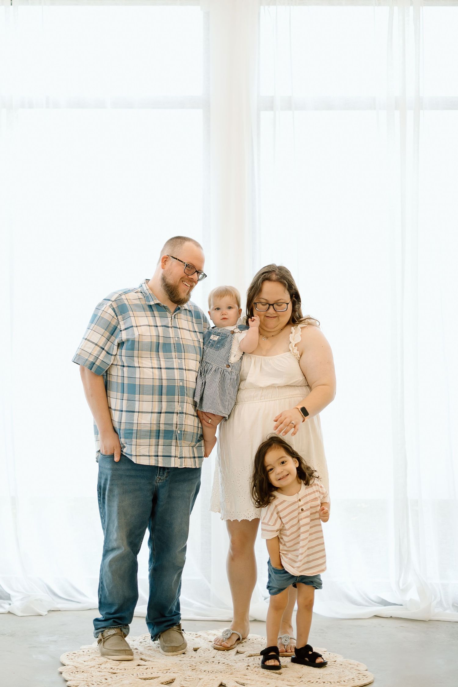 A family poses together in a bright white studio setting wearing casual clothing in three similar poses.