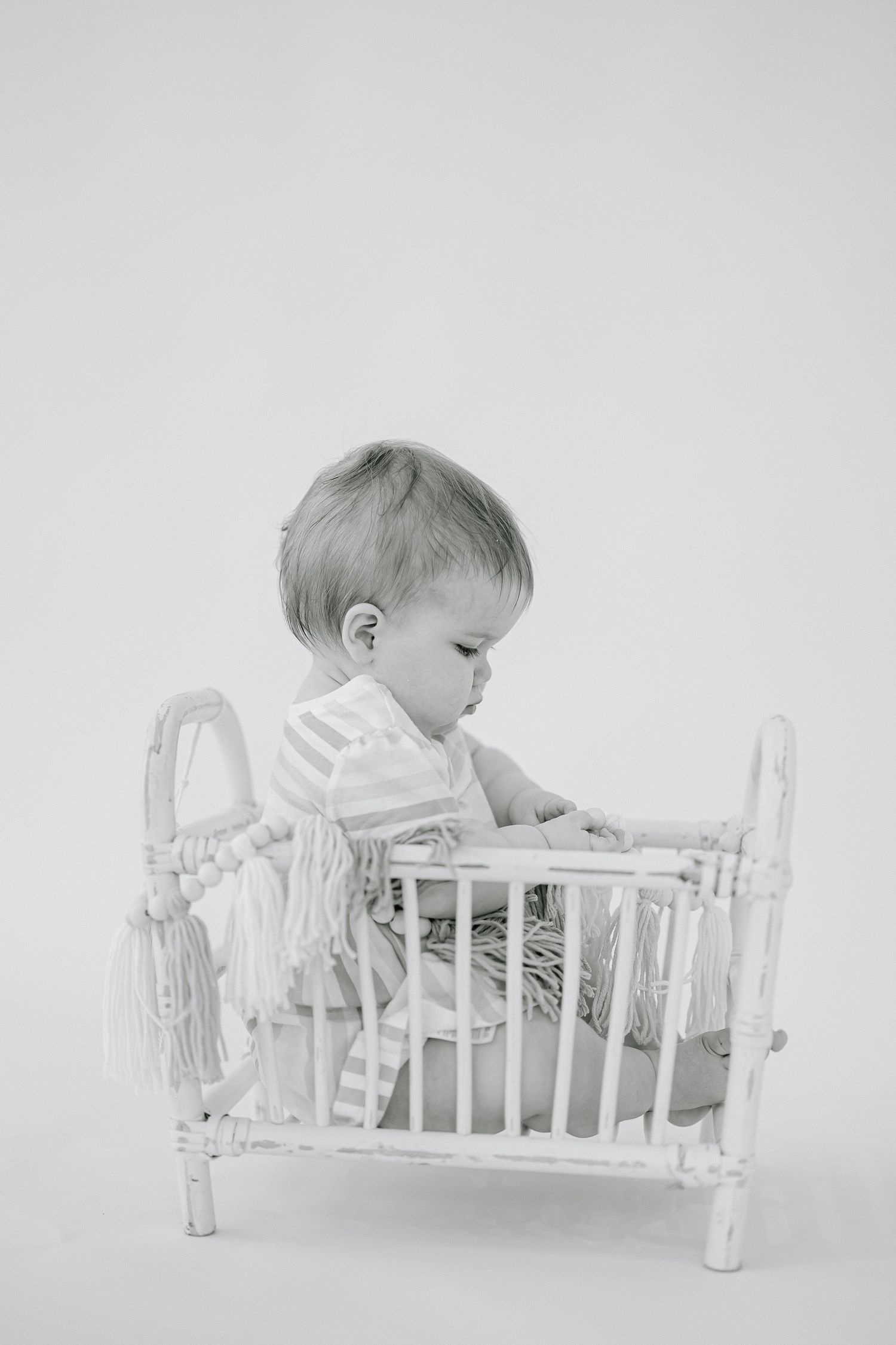 Series of black and white photos showing a small child lying in a white wooden doll bed.