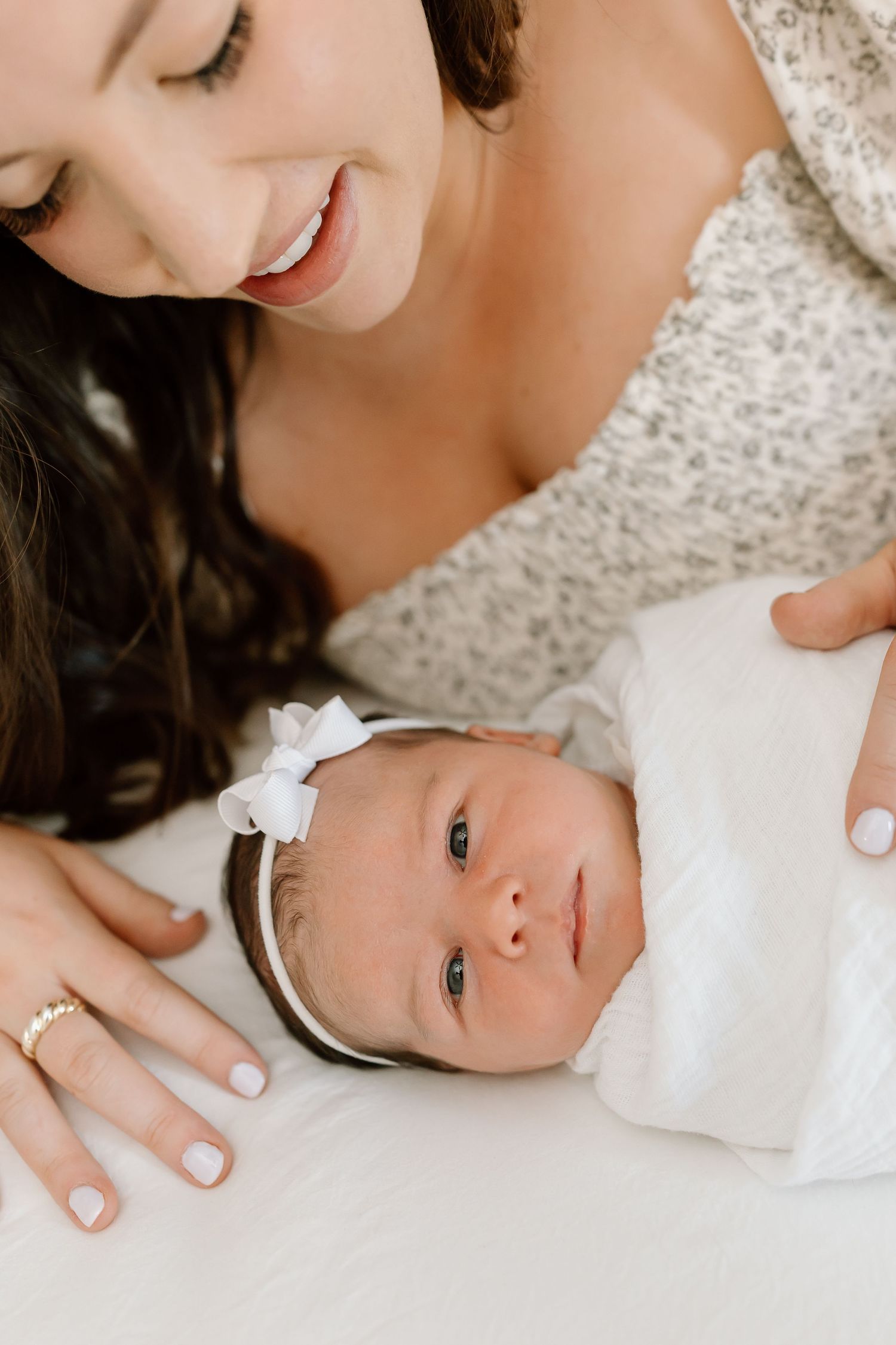 A tender moment between parent and baby as they lay together on a soft white surface.