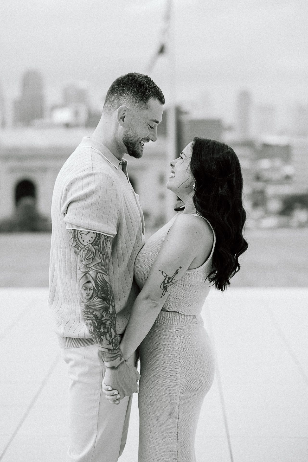 A romantic black and white photo series showing a couple in white outfits embracing on a rooftop with a city skyline backdrop.