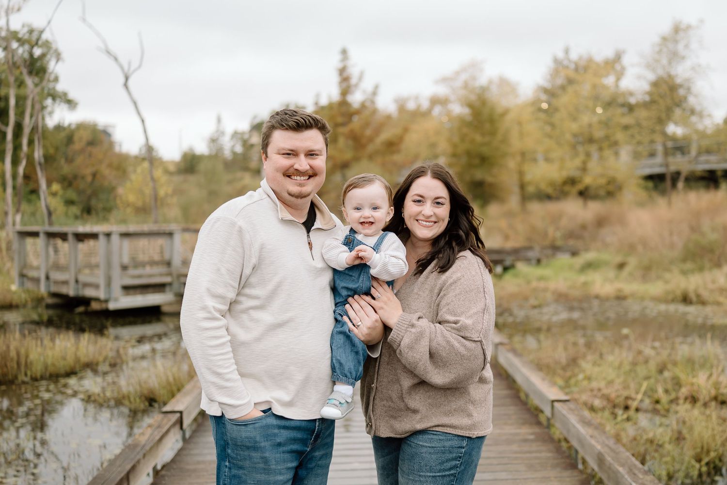 A family enjoys a tender moment together while walking along a wooden boardwalk in an autumn landscape.